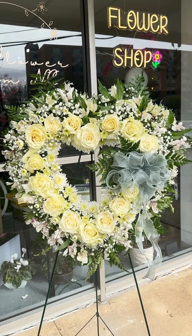 Forever in Our Hearts standing spray  - Our floral heart spray features a beautiful arrangement of white roses and white flowers, symbolizing love, purity, and serenity. With its heart-shaped wreath design, this elegant and comforting display serves as a touching tribute to honor and remember your loved ones. The combination of white roses and white flowers, accompanied by lush greenery, creates a harmonious blend of colors and textures, offering solace and peace during difficult times. "Forever in Our Hearts" is the perfect choice to convey your heartfelt condolences and provide comfort to those in mourning.