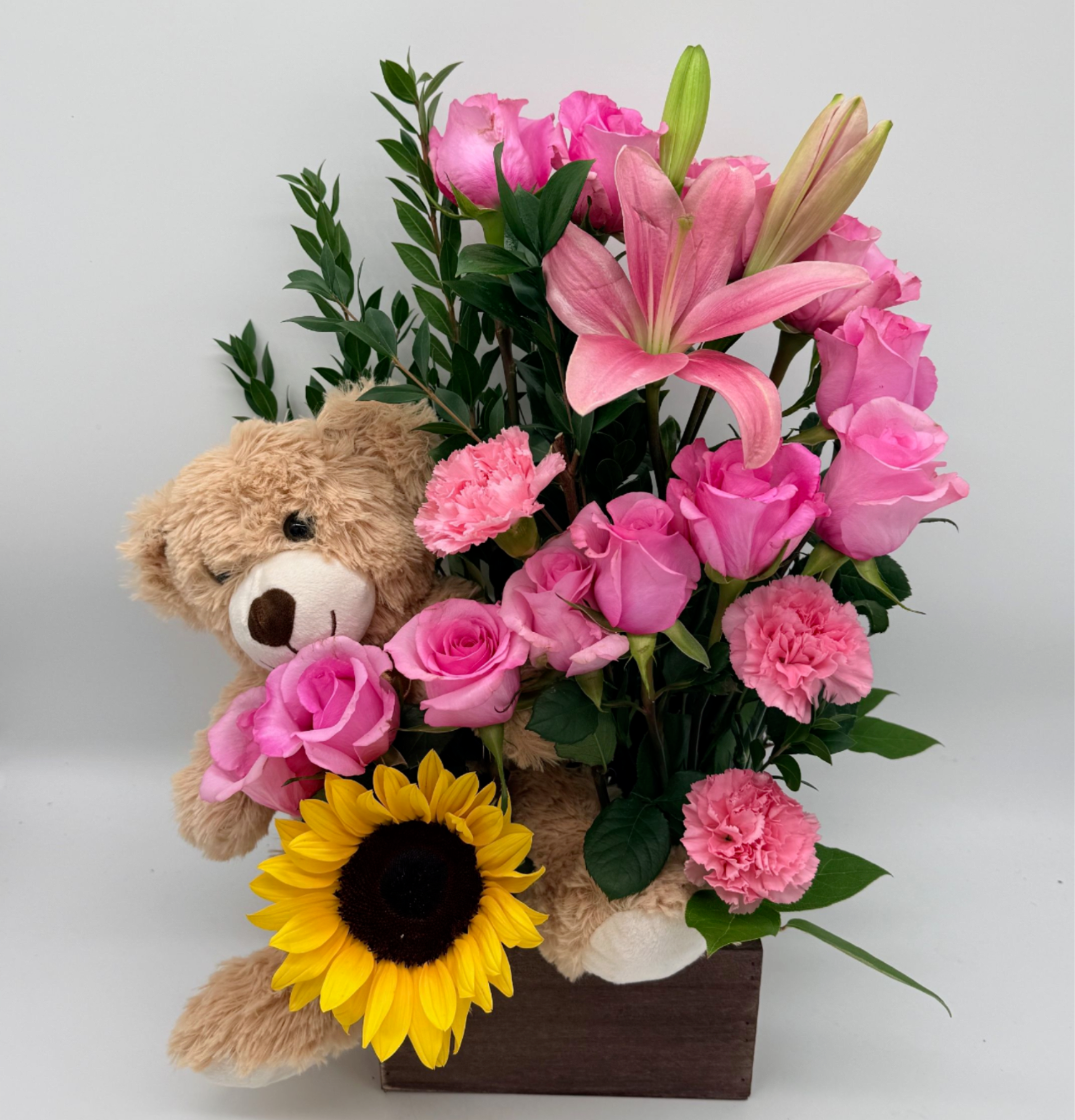 Pink roses and lilies arranged with a teddy bear and sunflower in a wooden box