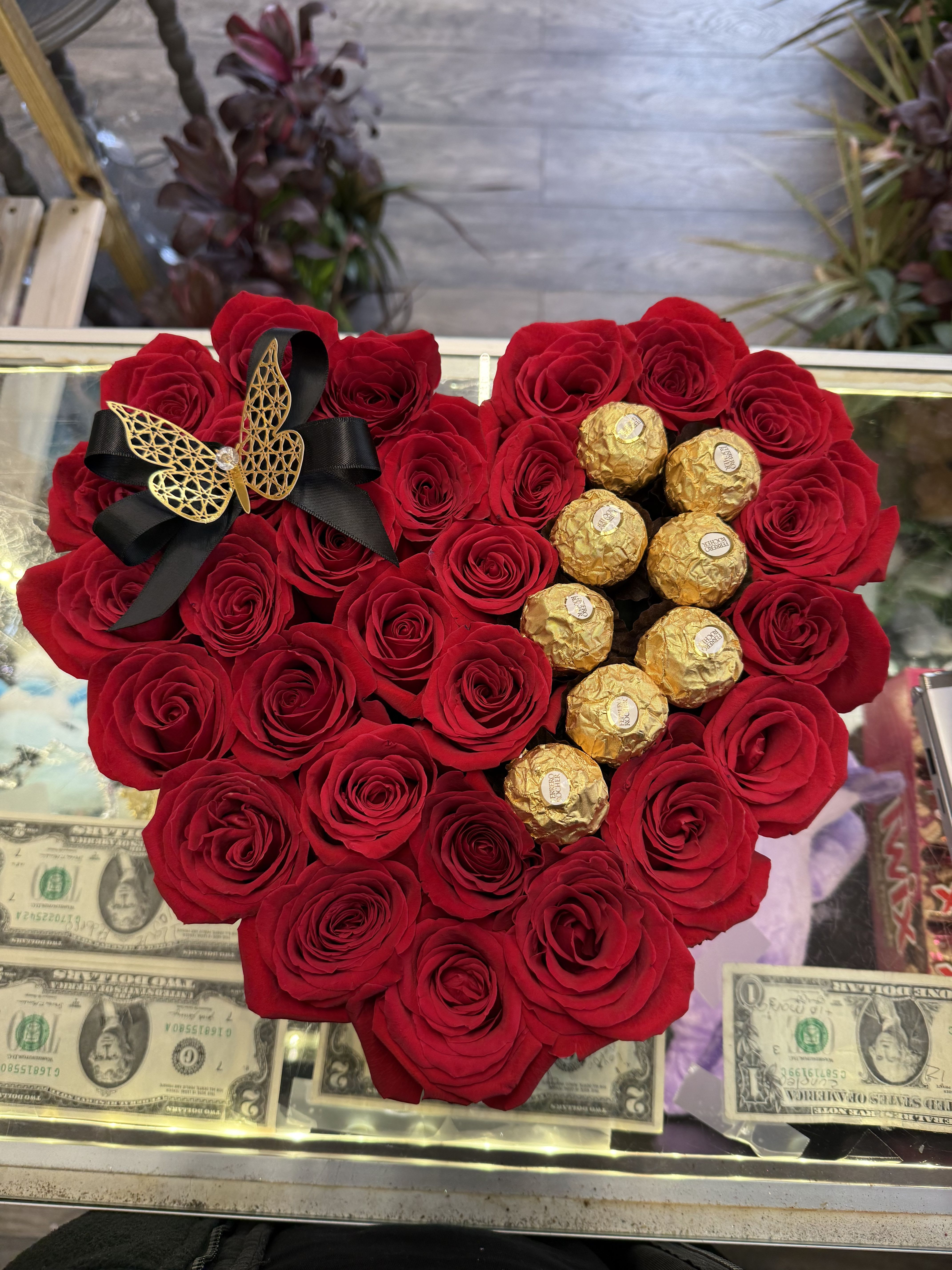 Heart-shaped red rose arrangement with gold-wrapped chocolates and a black ribbon bow