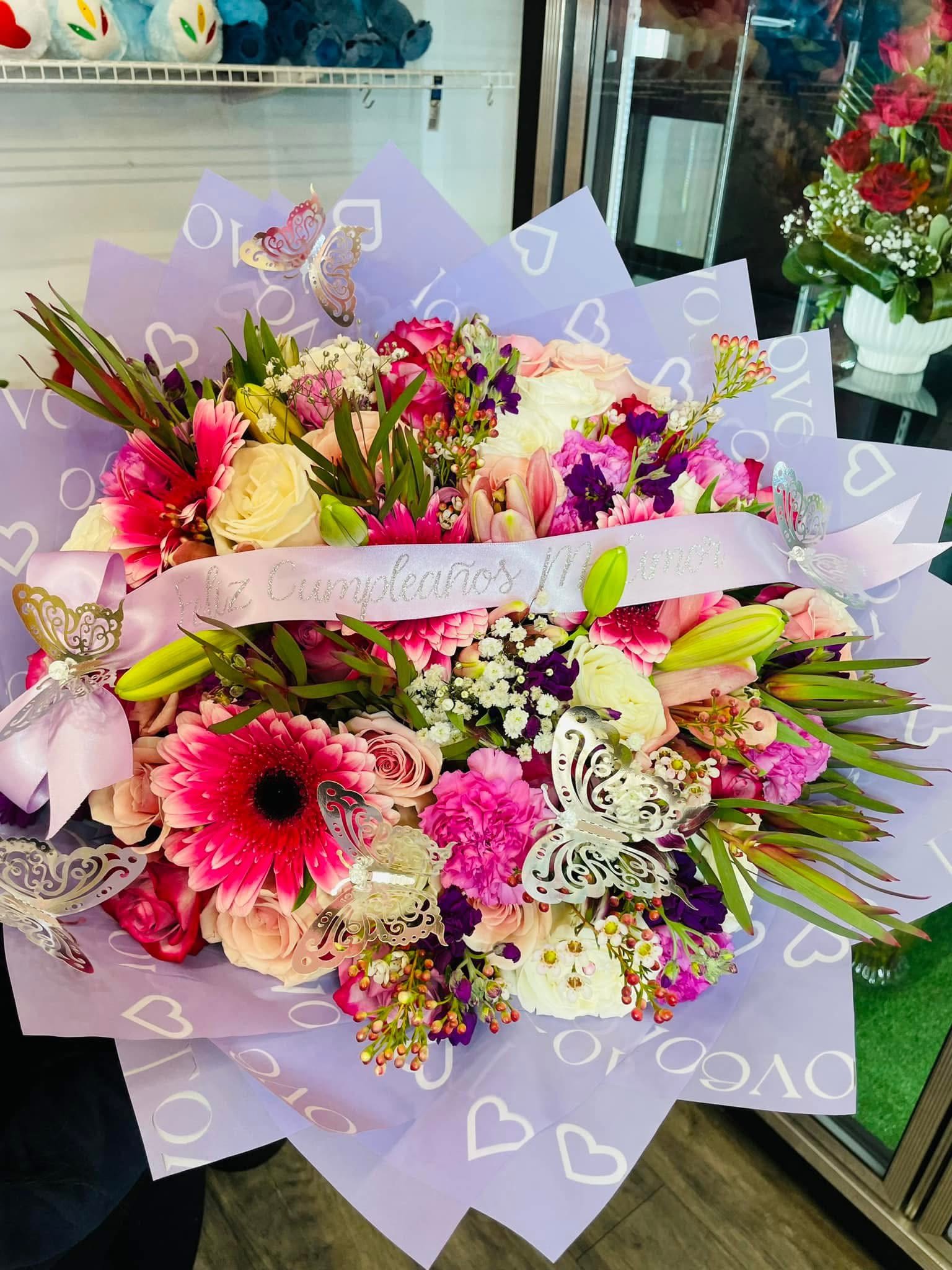 Large bouquet of pink, white, and peach flowers wrapped in lavender paper
