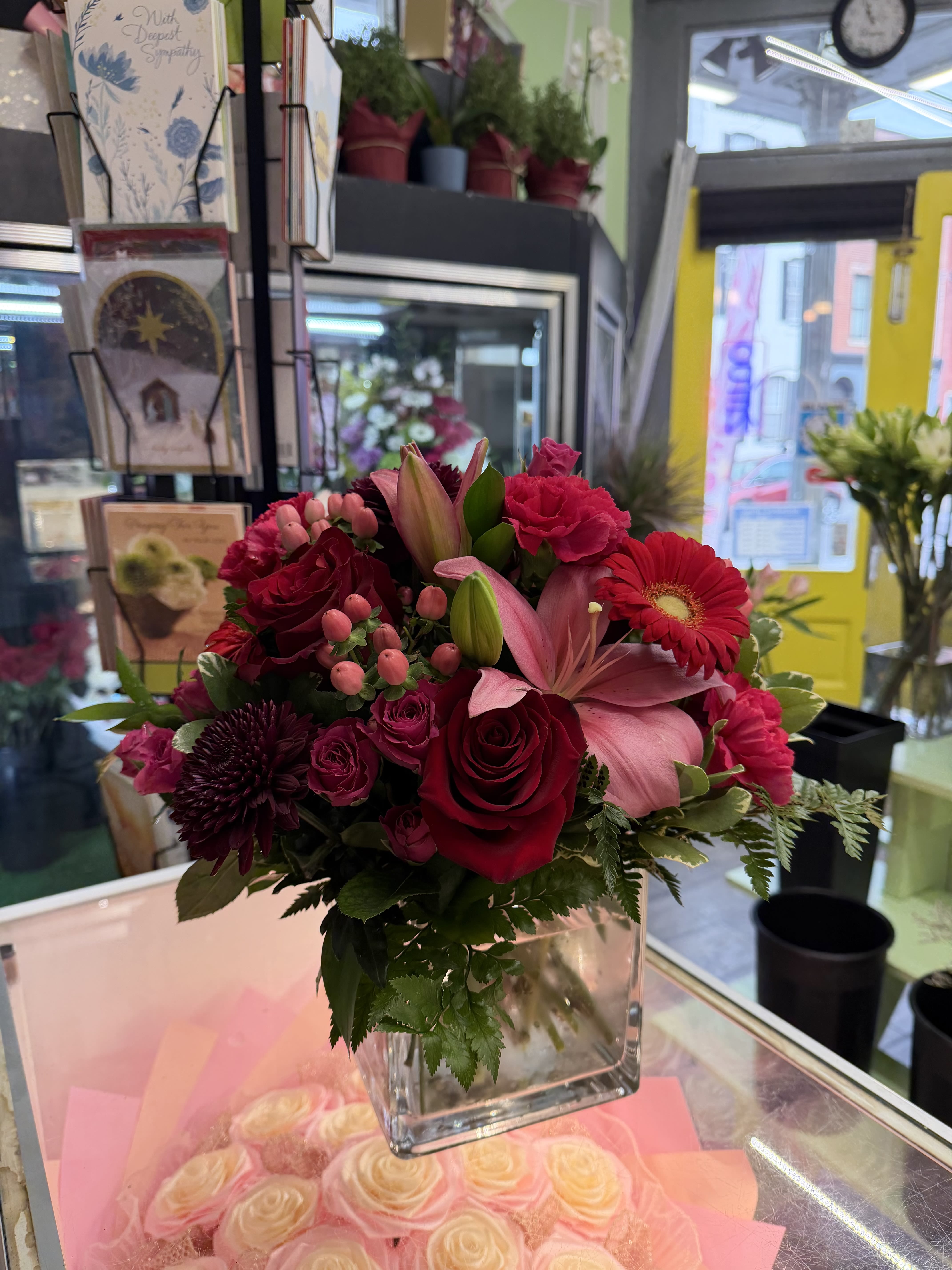 Mixed bouquet of red, pink, and burgundy flowers in a clear square vase