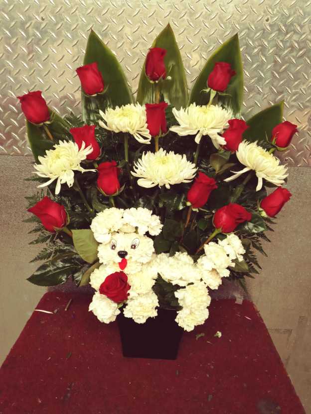 Red roses and white chrysanthemums arranged around a teddy bear in a black vase