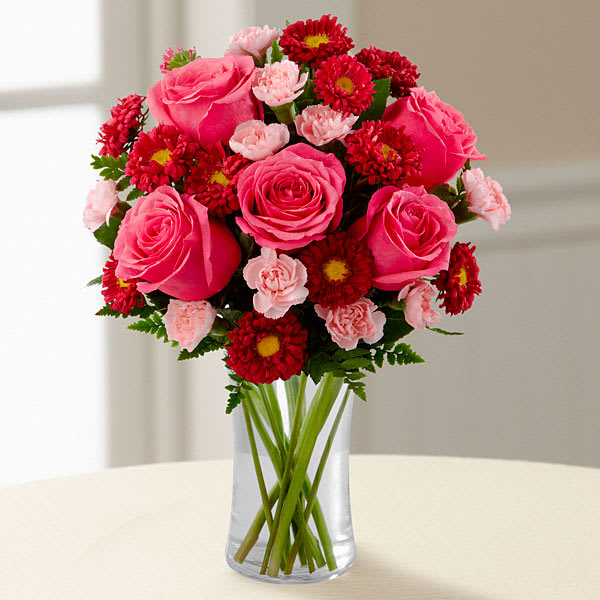 The FTD Precious Heart Bouquet - The FTD Precious Heart Bouquet is a blushing display of loving kindness. Fuchsia roses are sweetly stunning amongst red matsumoto asters pink mini carnations and lush greens. Arranged in a classic clear glass vase this bouquet boasts pink perfection to convey your warmest wishes.