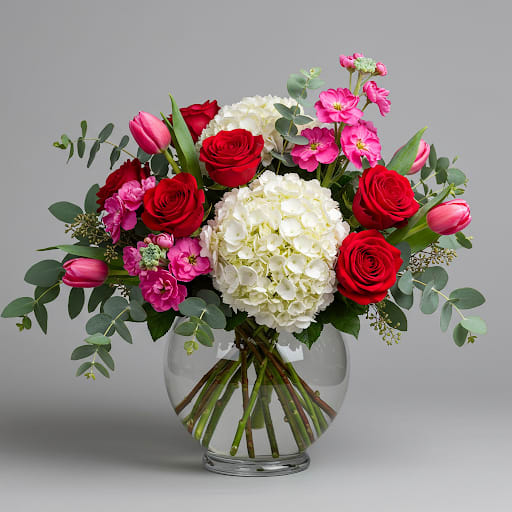 Bouquet of red roses, white hydrangeas, and pink tulips in a glass vase
