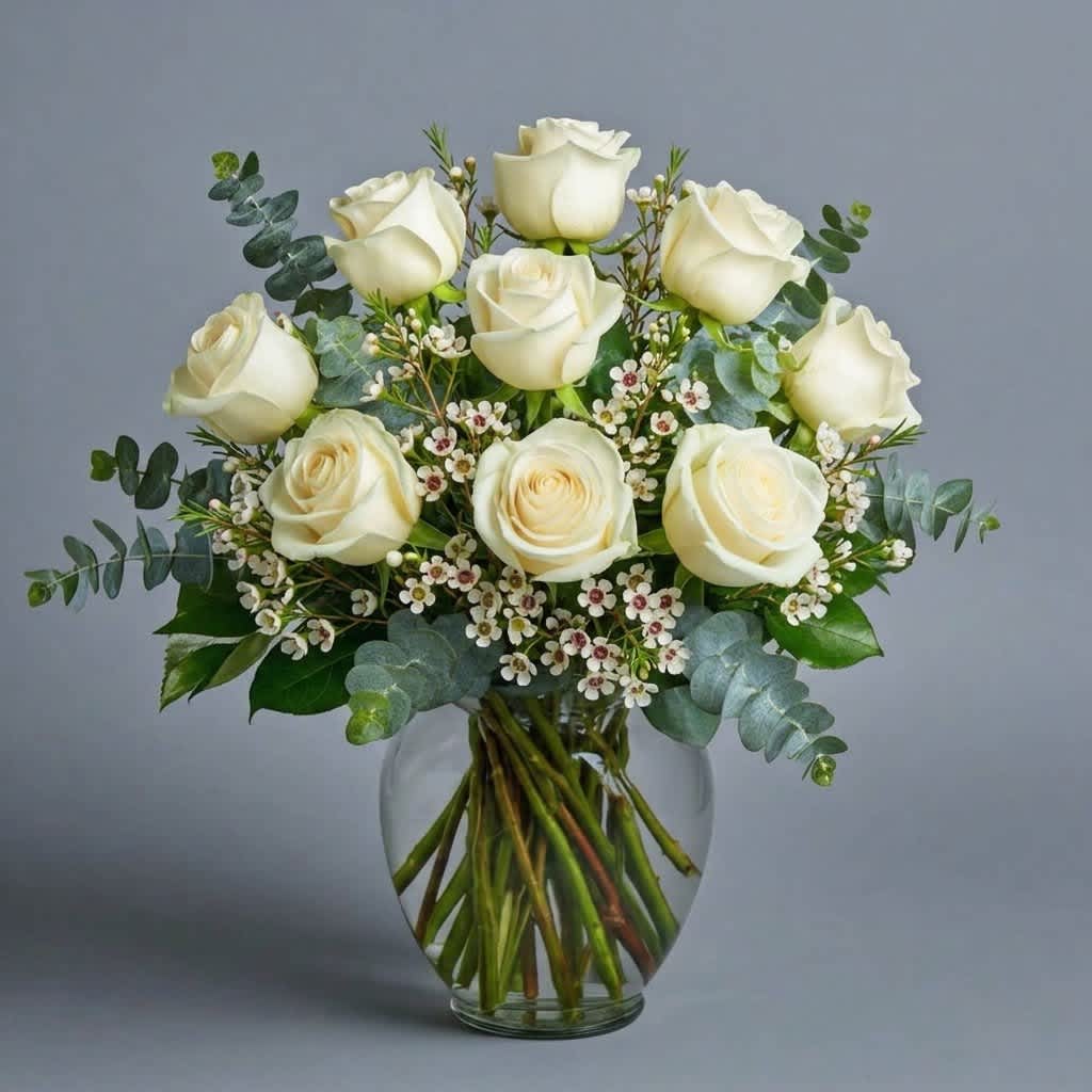 White roses arranged in a clear glass vase with small white filler flowers