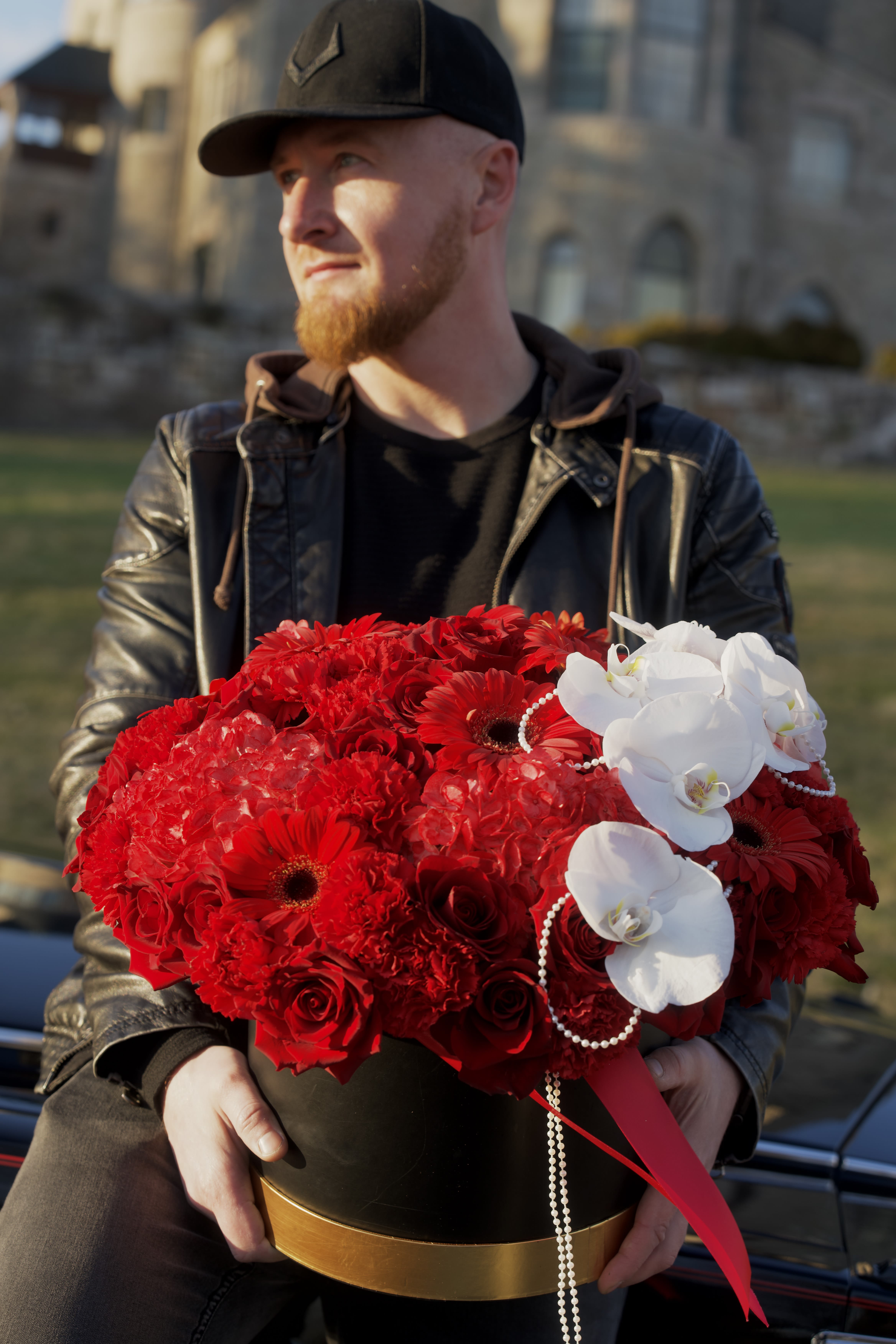 Large red floral arrangement in a black hatbox with white orchids and pearl strands