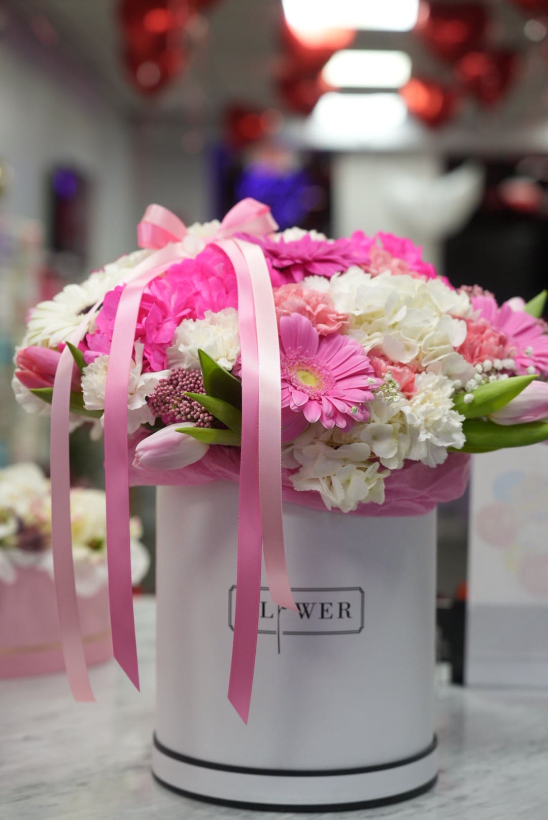 Pink and white flower arrangement in a white hatbox with ribbon