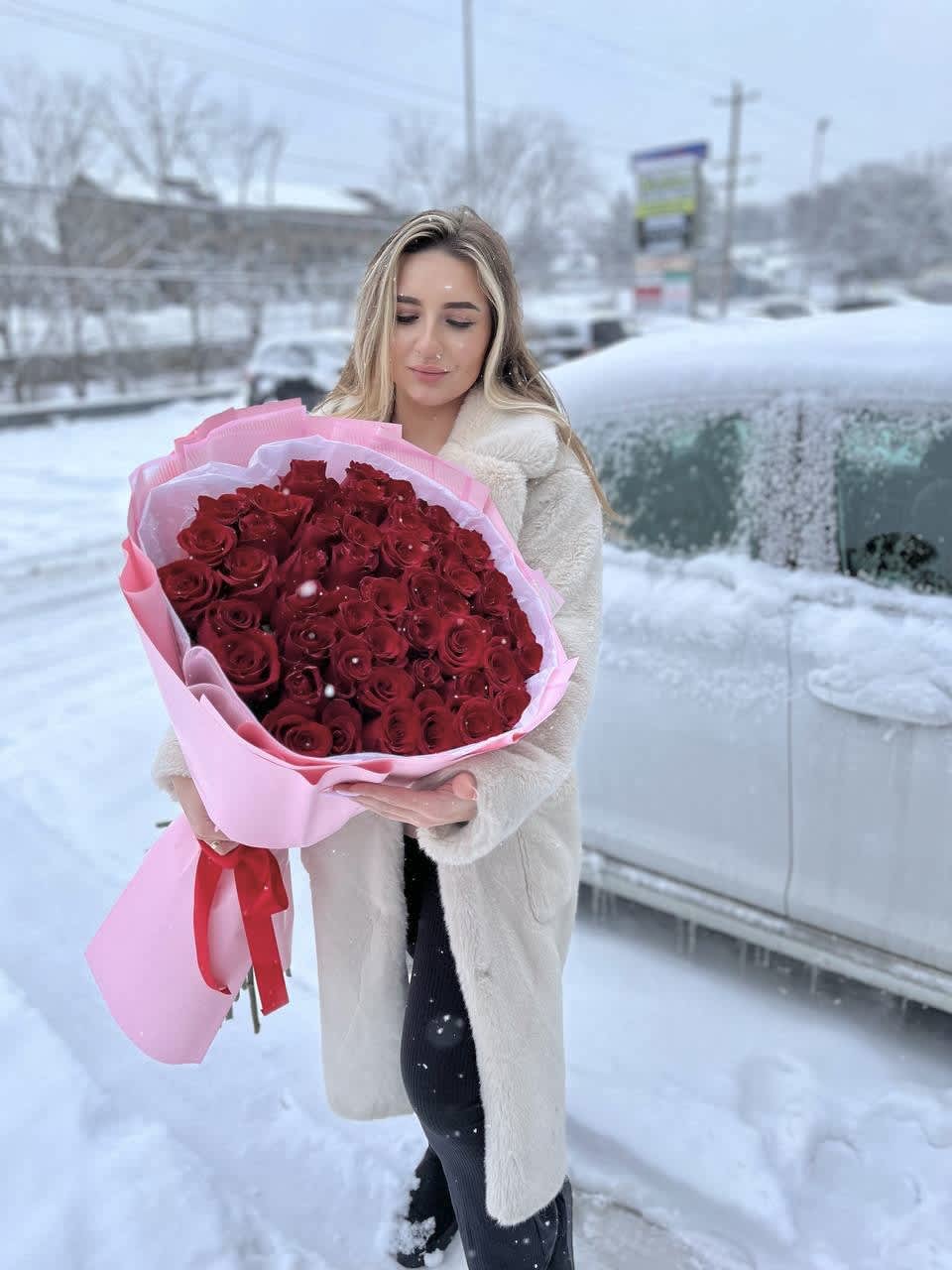 Woman holding a large bouquet of red roses wrapped in pink paper