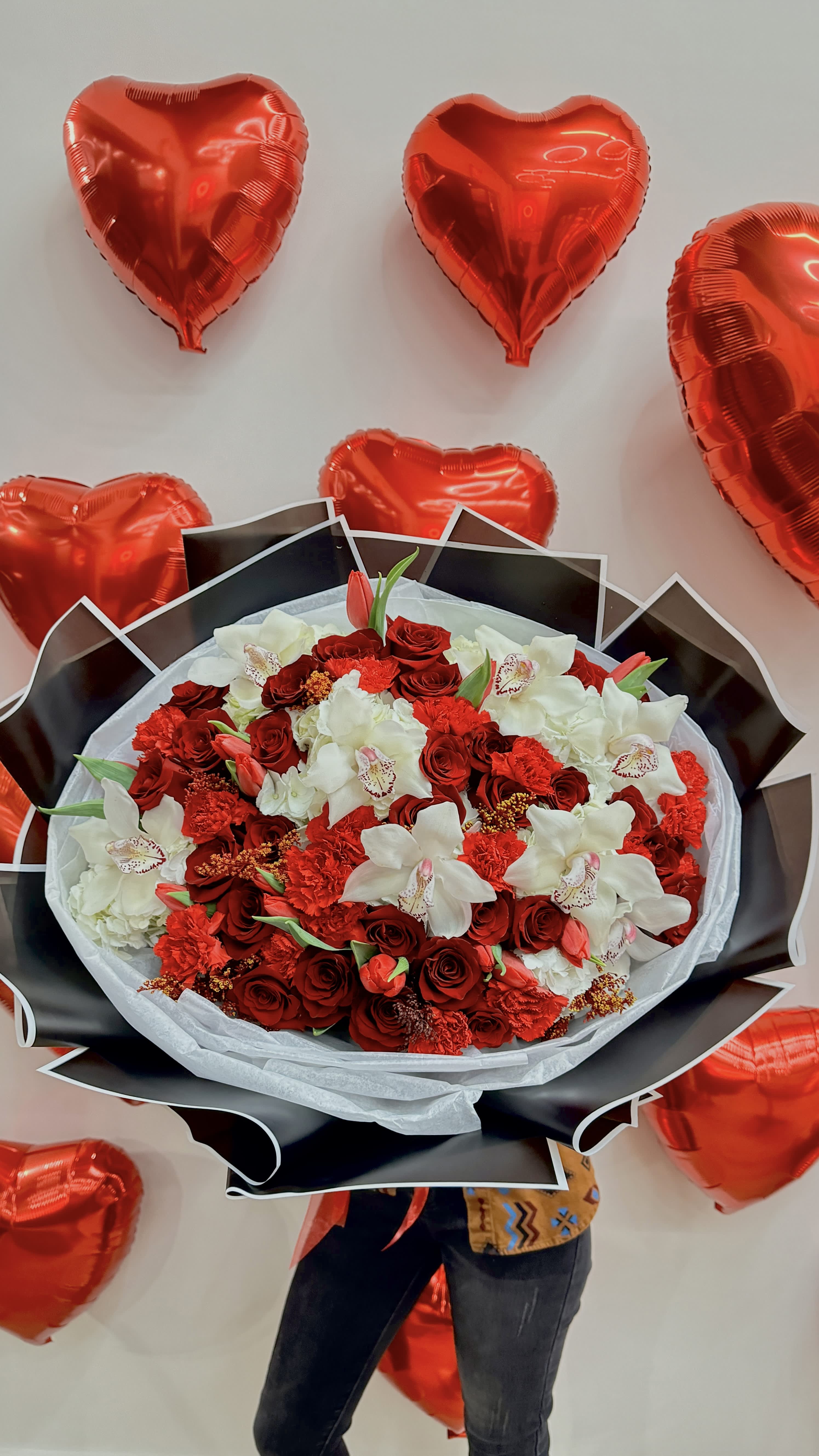 Red and white bouquet surrounded by red heart balloons