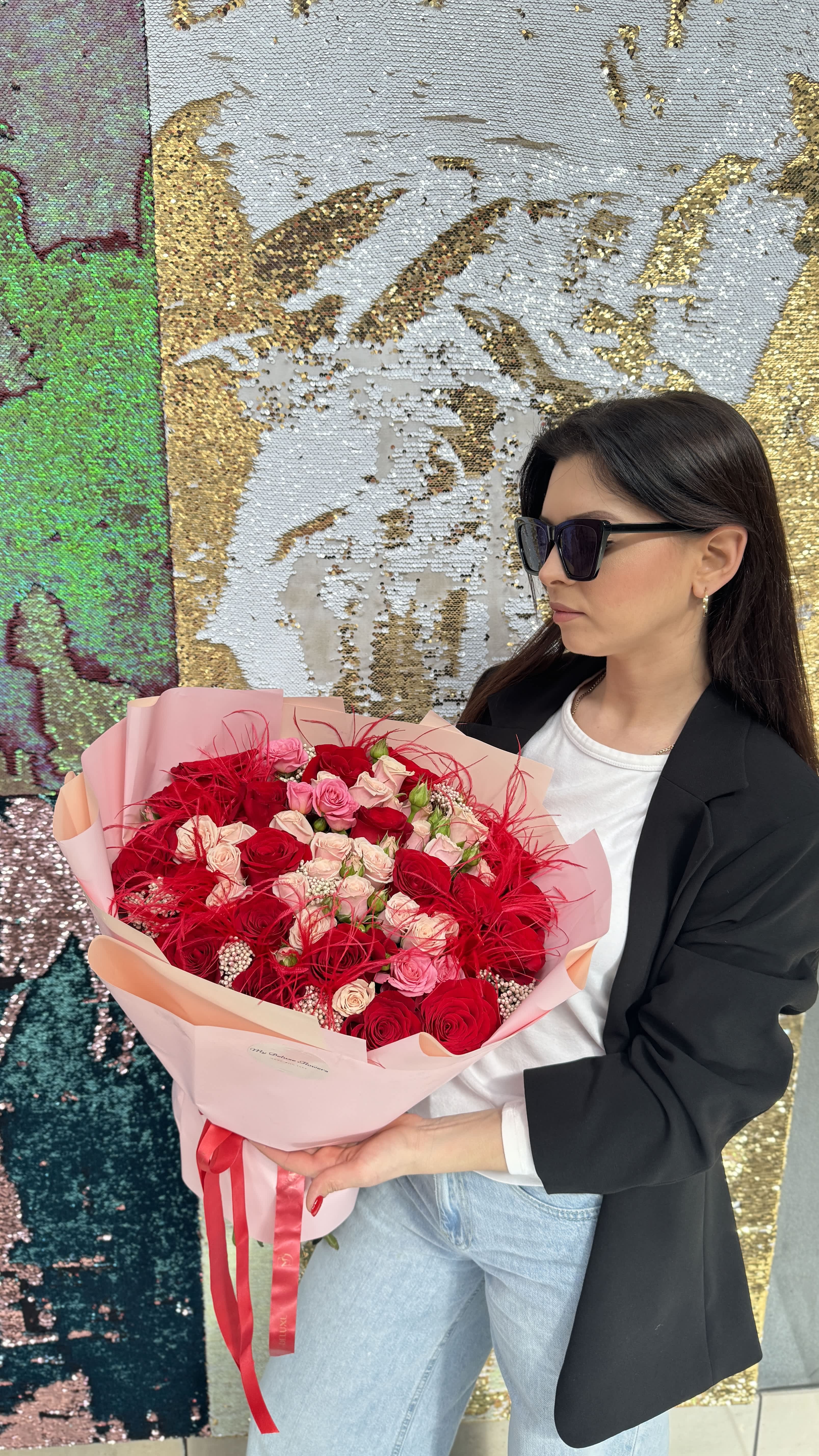 Woman holding a large bouquet of red and pink roses wrapped in pale pink paper
