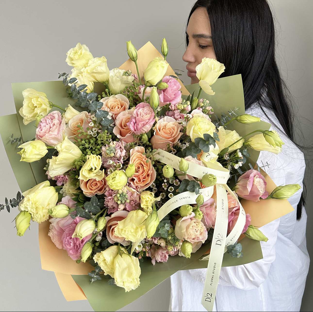 Large bouquet of pale yellow and peach flowers wrapped in green and peach paper