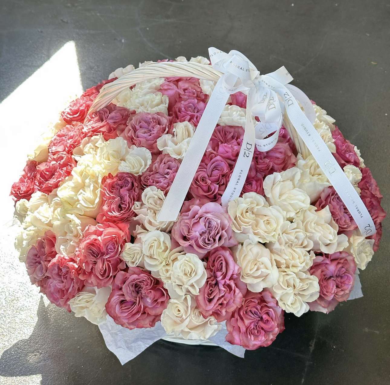 Round basket filled with pink and cream roses tied with white ribbons