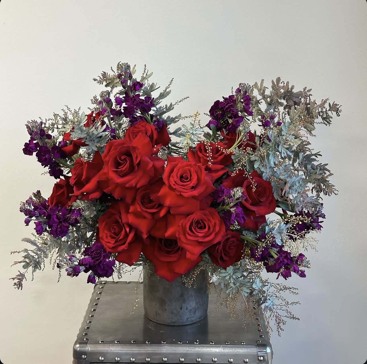 Melissa  - This striking vased arrangement combines the classic beauty of red roses with rich,deep hues of purple stock flowers. Together, they create a harmonious and sophisticated bouquet that is sure to make a statement.