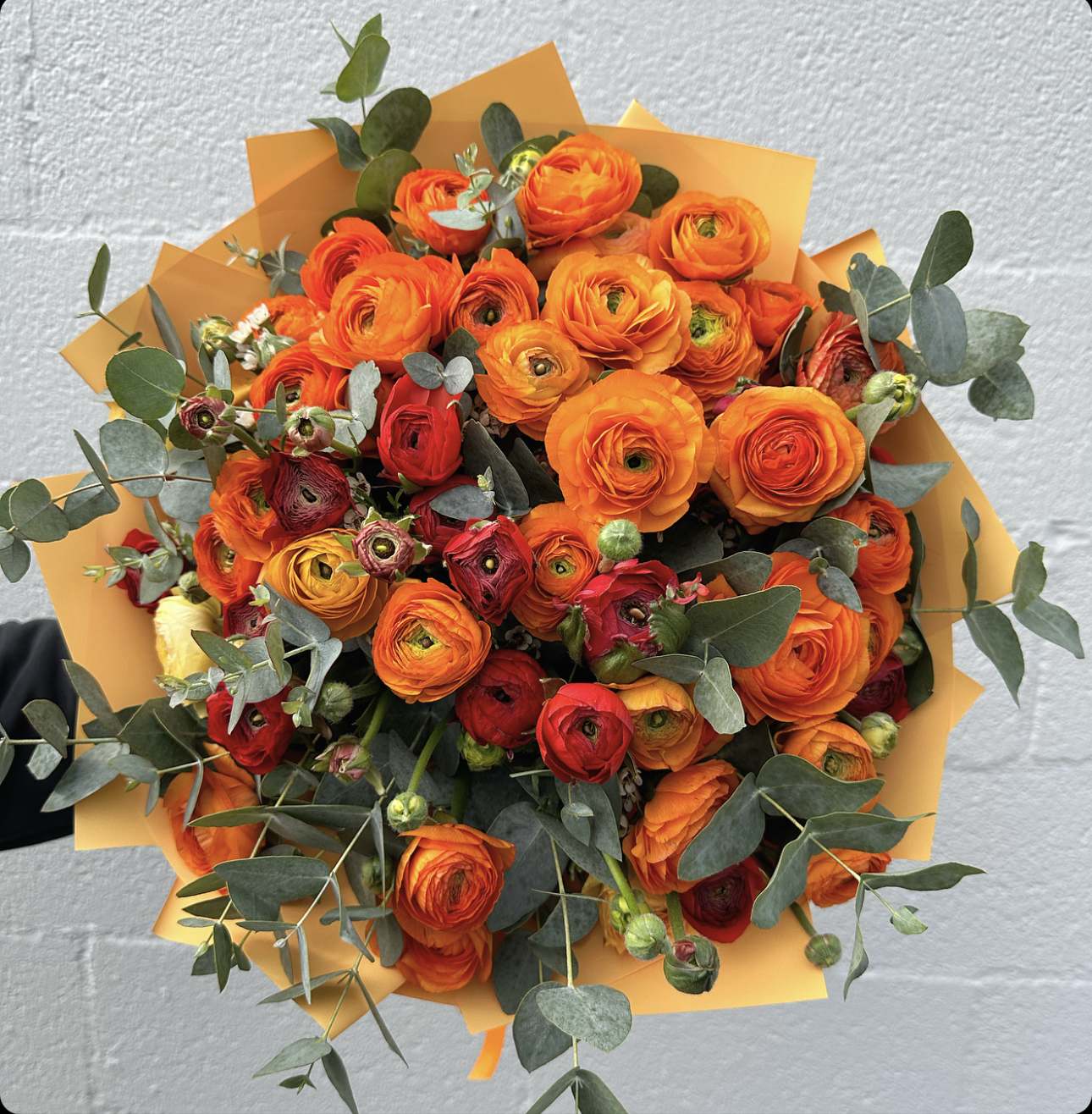 Bouquet of orange and red ranunculus with eucalyptus in orange wrap