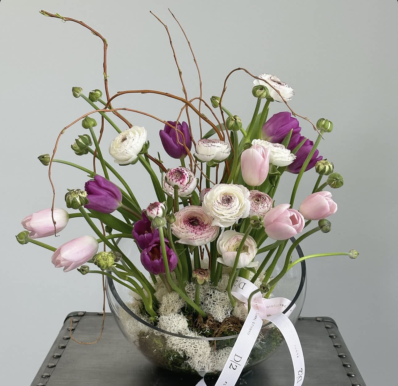 Mixed tulips and ranunculus in a clear glass bowl with a ribbon