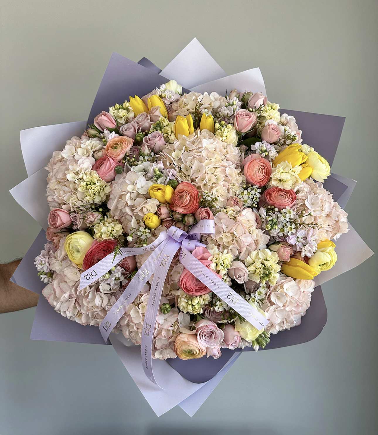 Large pastel bouquet of roses, hydrangeas, and yellow tulips wrapped in lavender paper