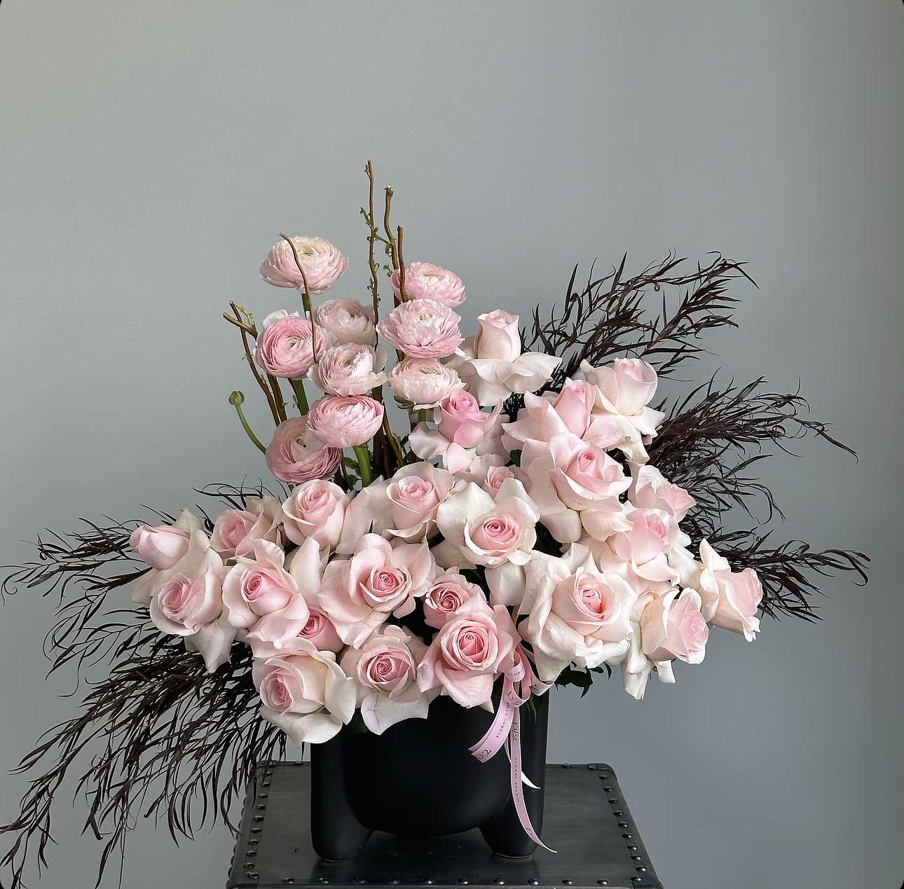 Pink roses and ranunculus in a black vase with dark feathery accents