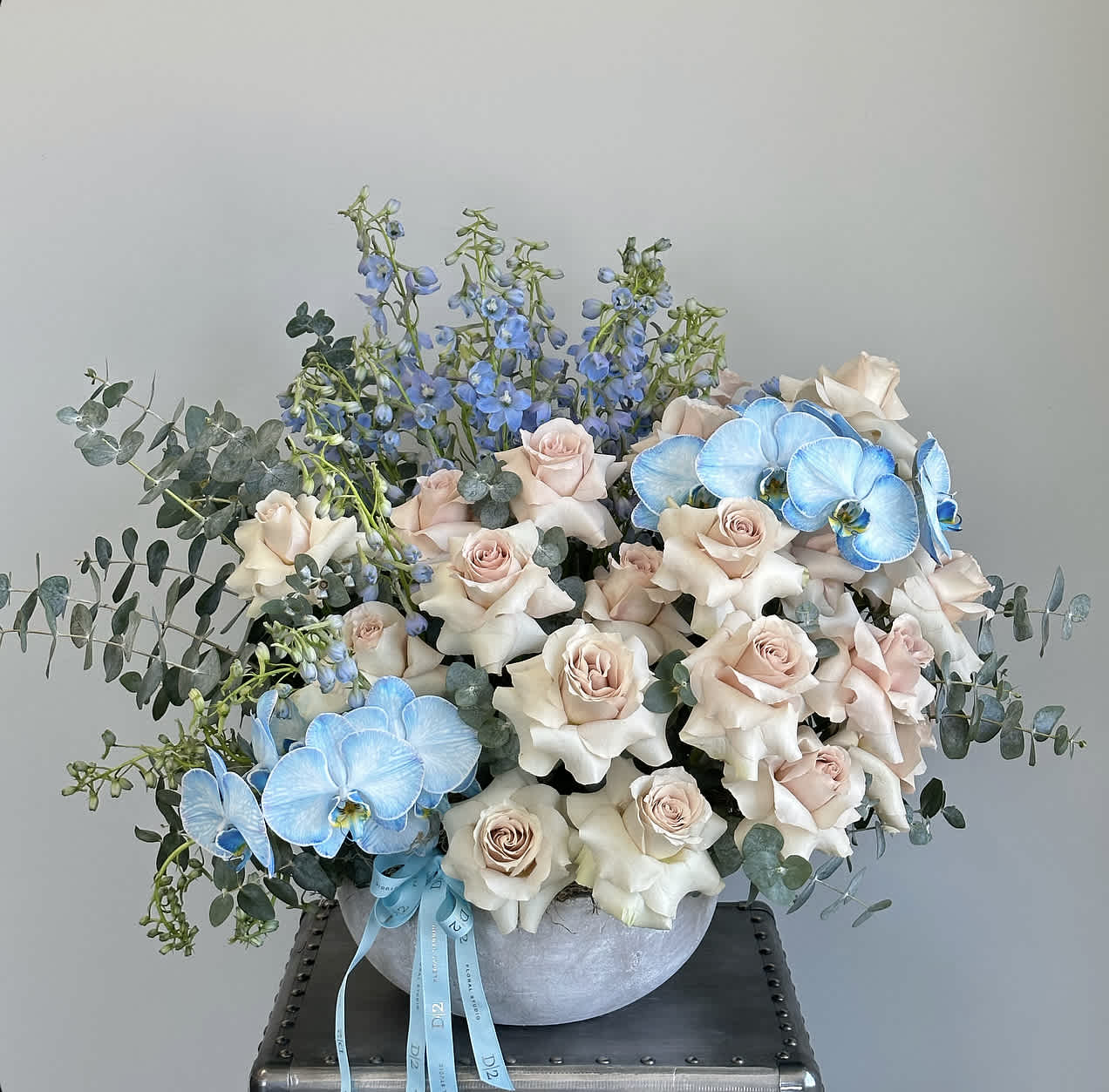 Cream roses and blue orchids in a round vase with eucalyptus