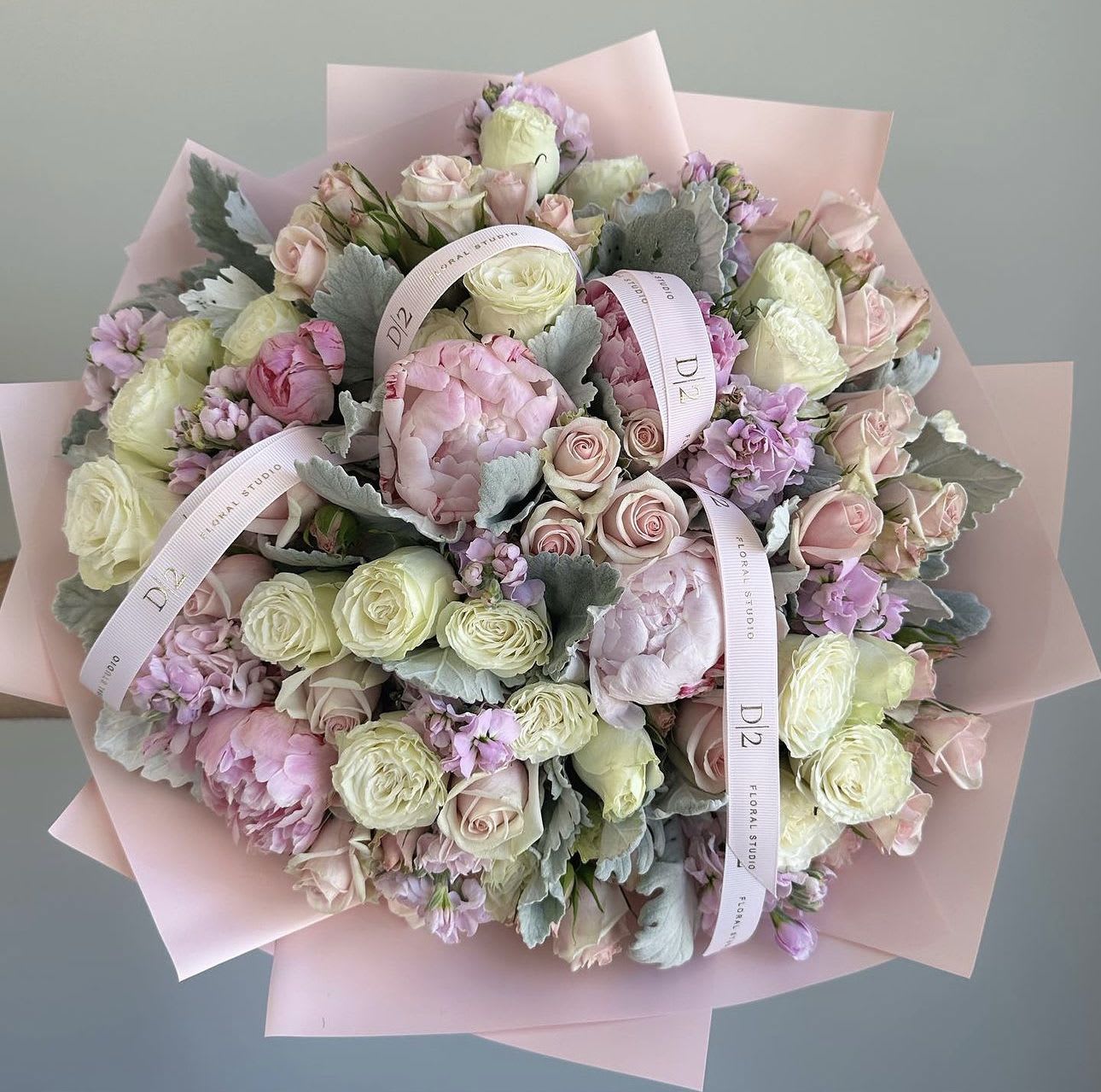 Bouquet of pale pink and cream roses with lavender blooms wrapped in pink paper