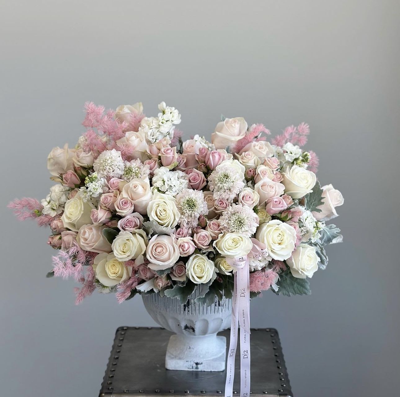 Large pastel bouquet of roses and white filler flowers in a white urn vase