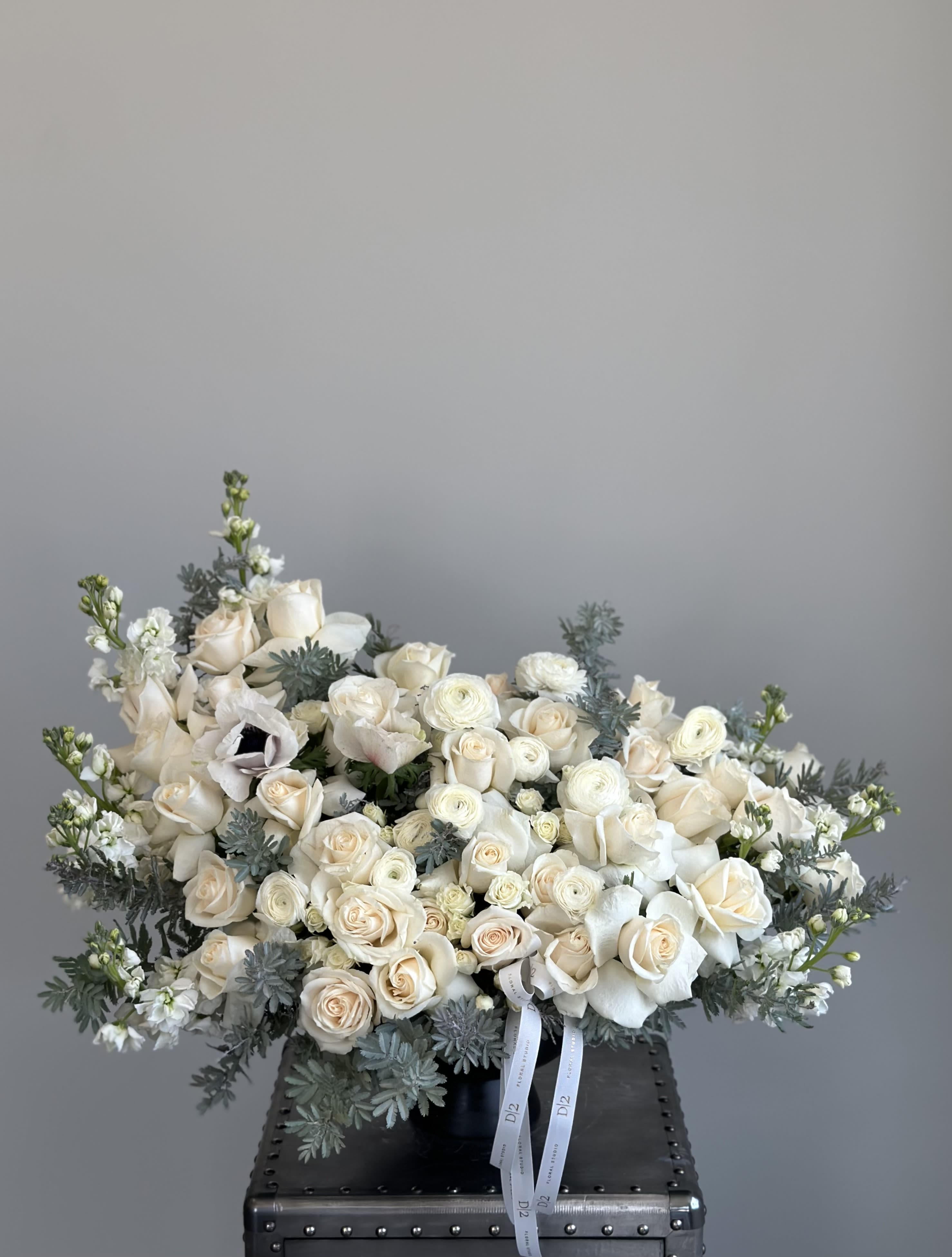 Cream rose bouquet with white blooms and blue-gray foliage in a black vase