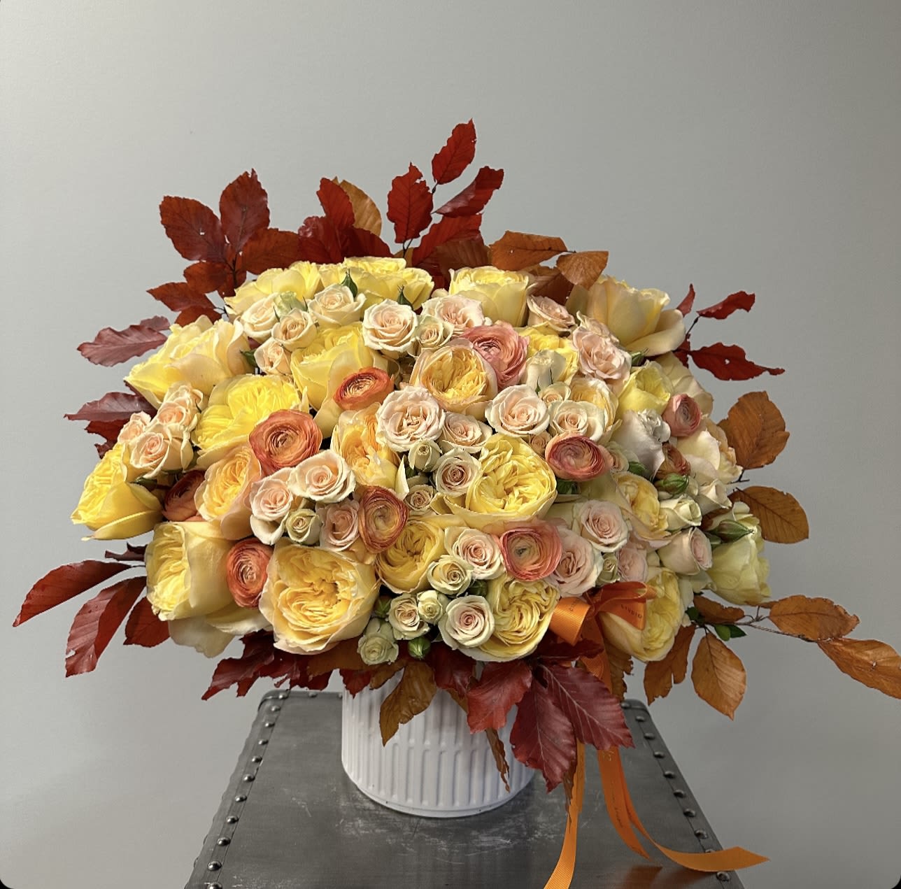 Large bouquet of yellow and peach roses in a white vase with autumn leaves