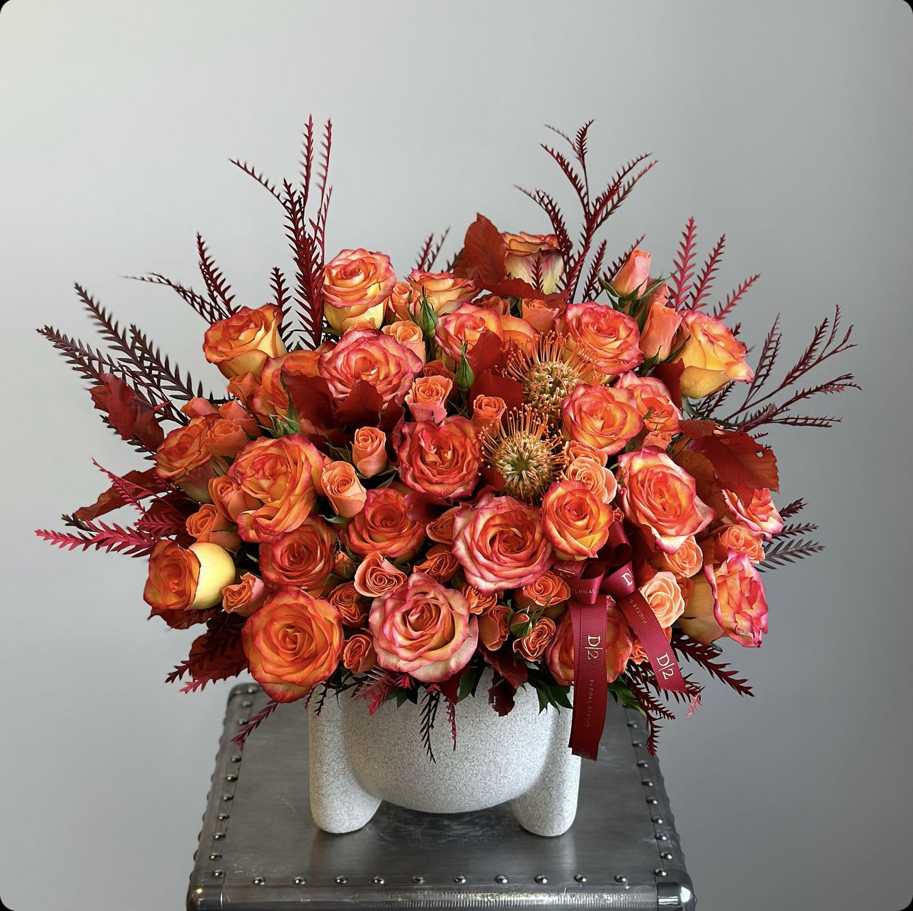 Agapi - A vase arrangement with orange roses and spray roses creates a stunning display of vibrant hues, complemented by lush greenery and delicate textures, offering a warm and elegant touch to any space.