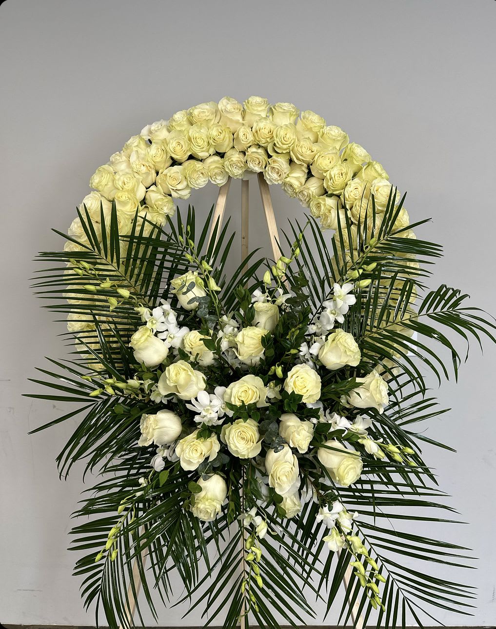 White rose funeral wreath with palm fronds and white orchids