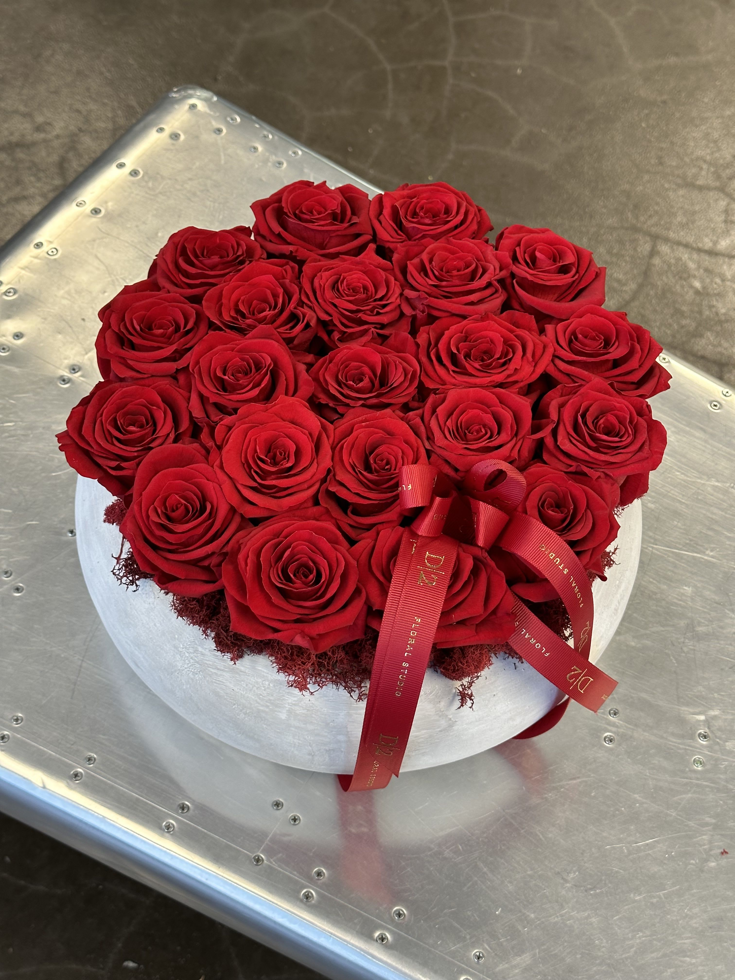Round arrangement of red roses in a white hat box with a red ribbon