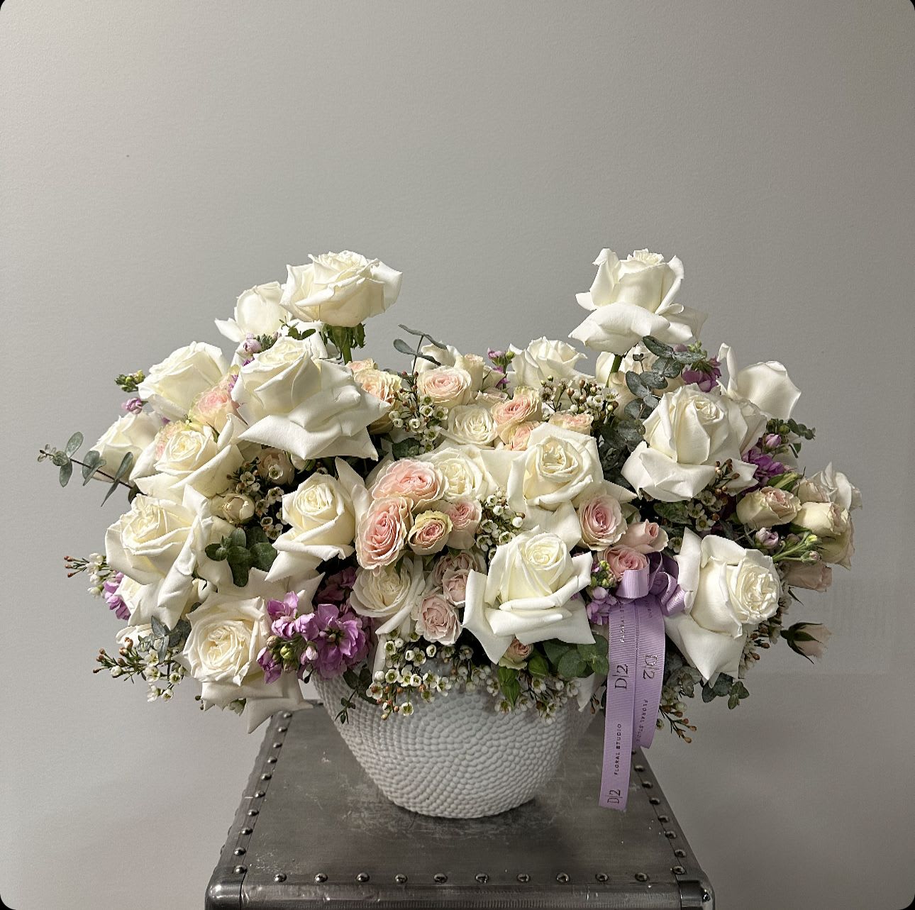 White rose arrangement in a textured white vase with a lavender ribbon