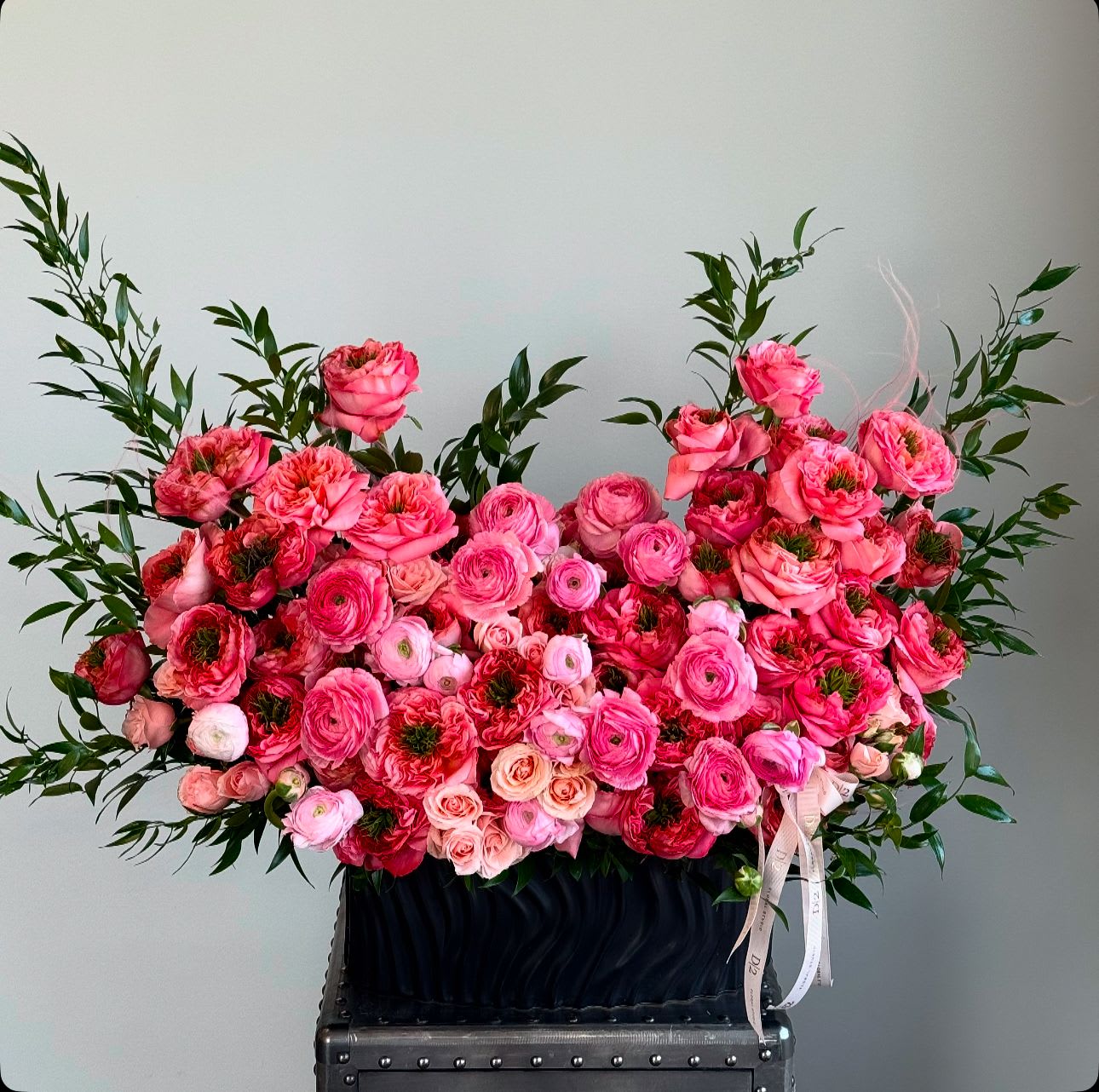 Large pink floral arrangement in a black container with ribbon