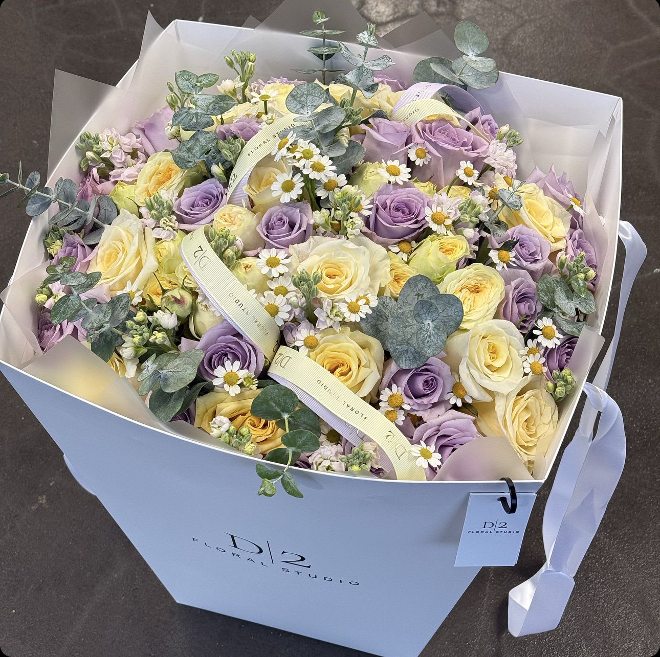 Bouquet of lavender and pale yellow roses with small white daisies in a gift box