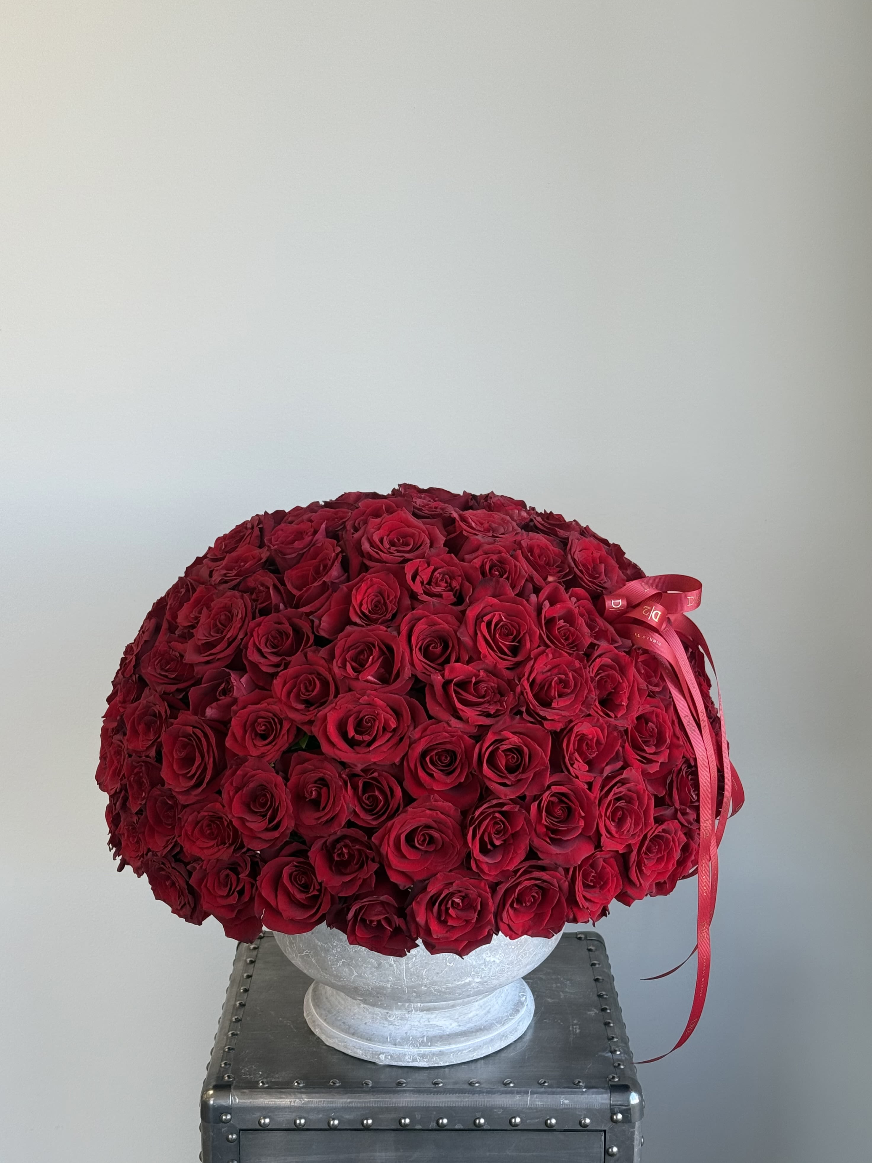 Large dome arrangement of red roses in a white pedestal vase with a red ribbon