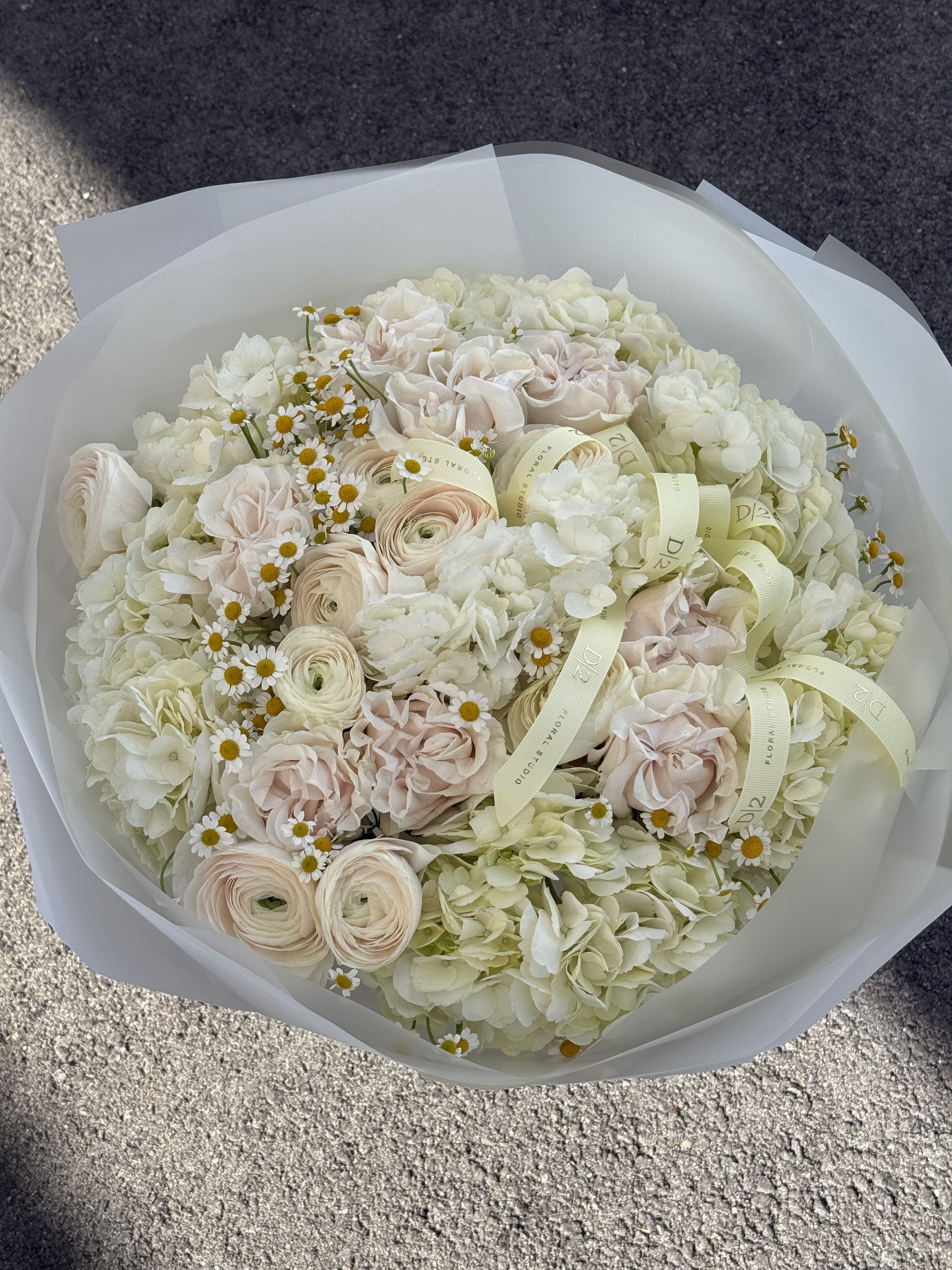 Bouquet of pale roses, ranunculus, hydrangeas, and small daisies wrapped in white paper