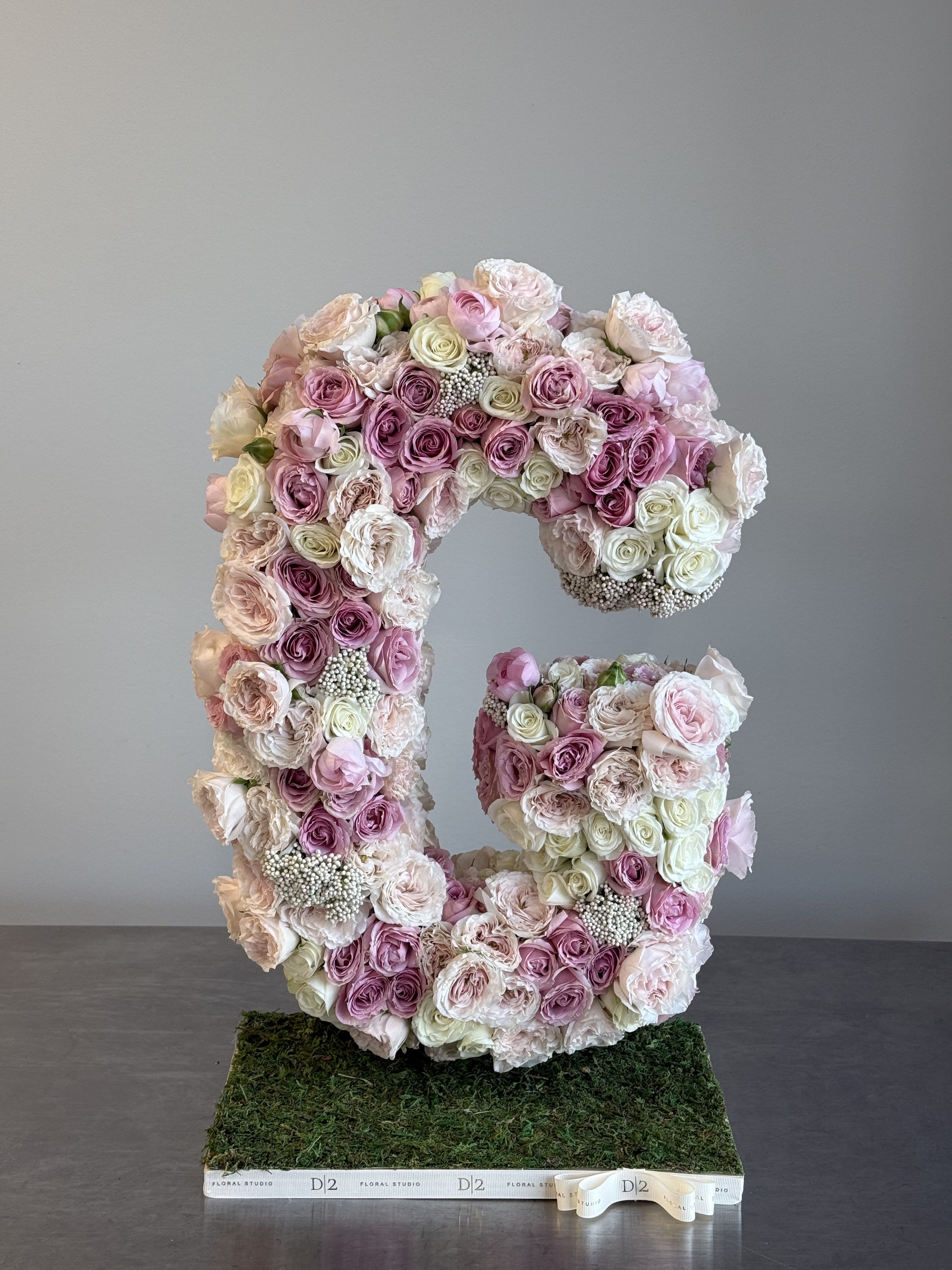 Large floral letter C made of pink and white roses on a moss base