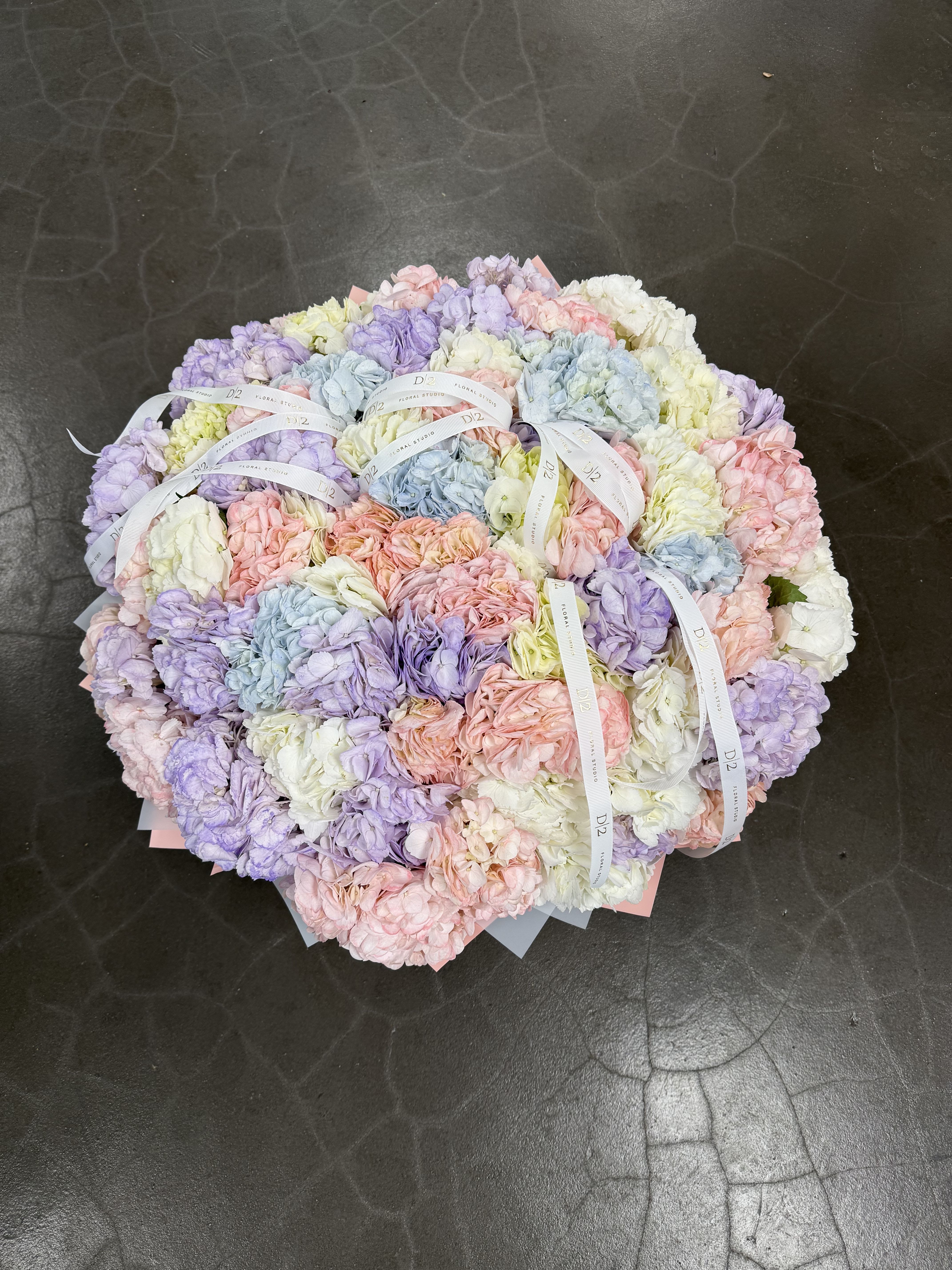 Pastel hydrangea bouquet with ribbon ties on a dark floor