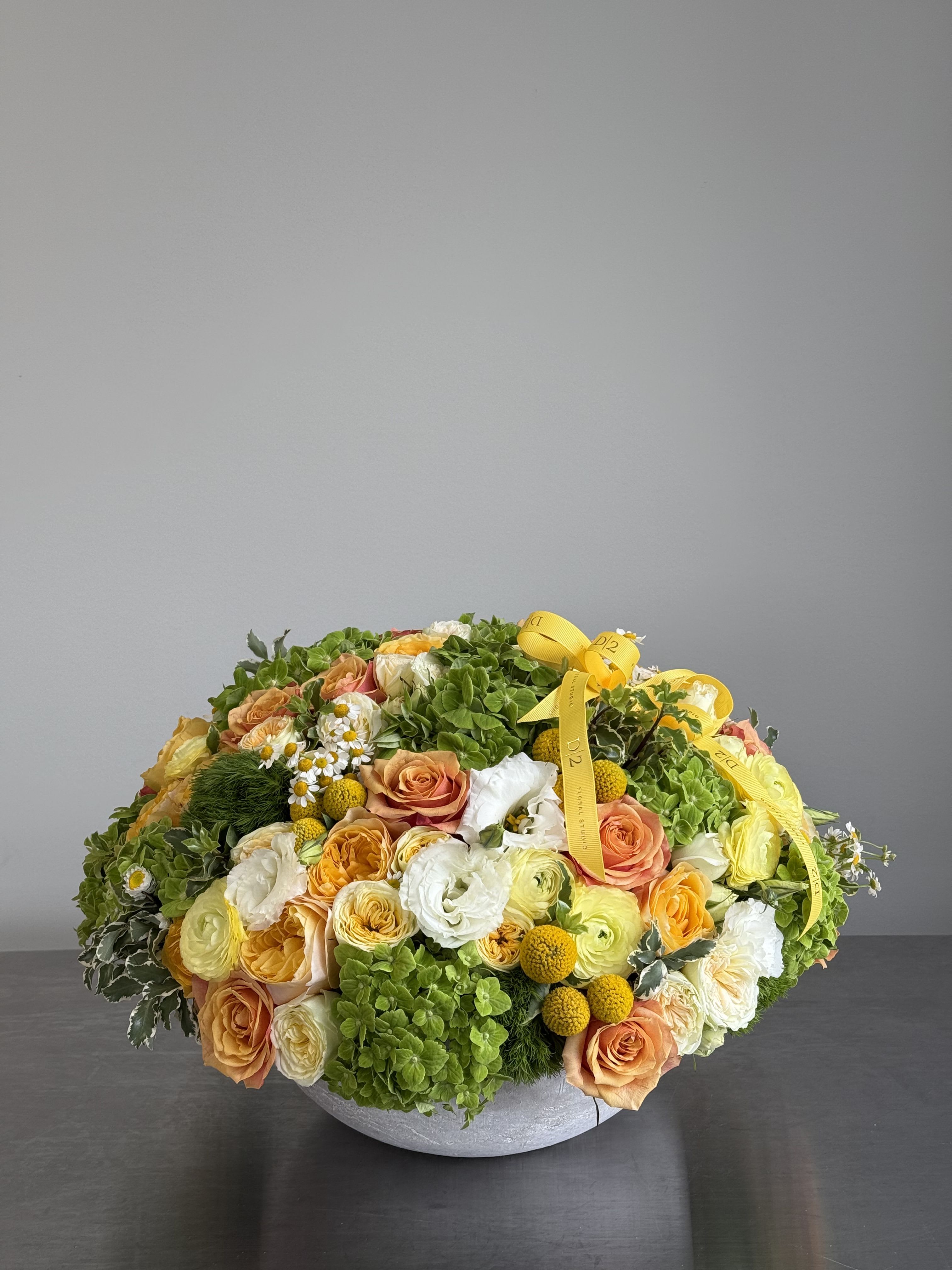 Round floral arrangement with peach and white roses in a low gray bowl