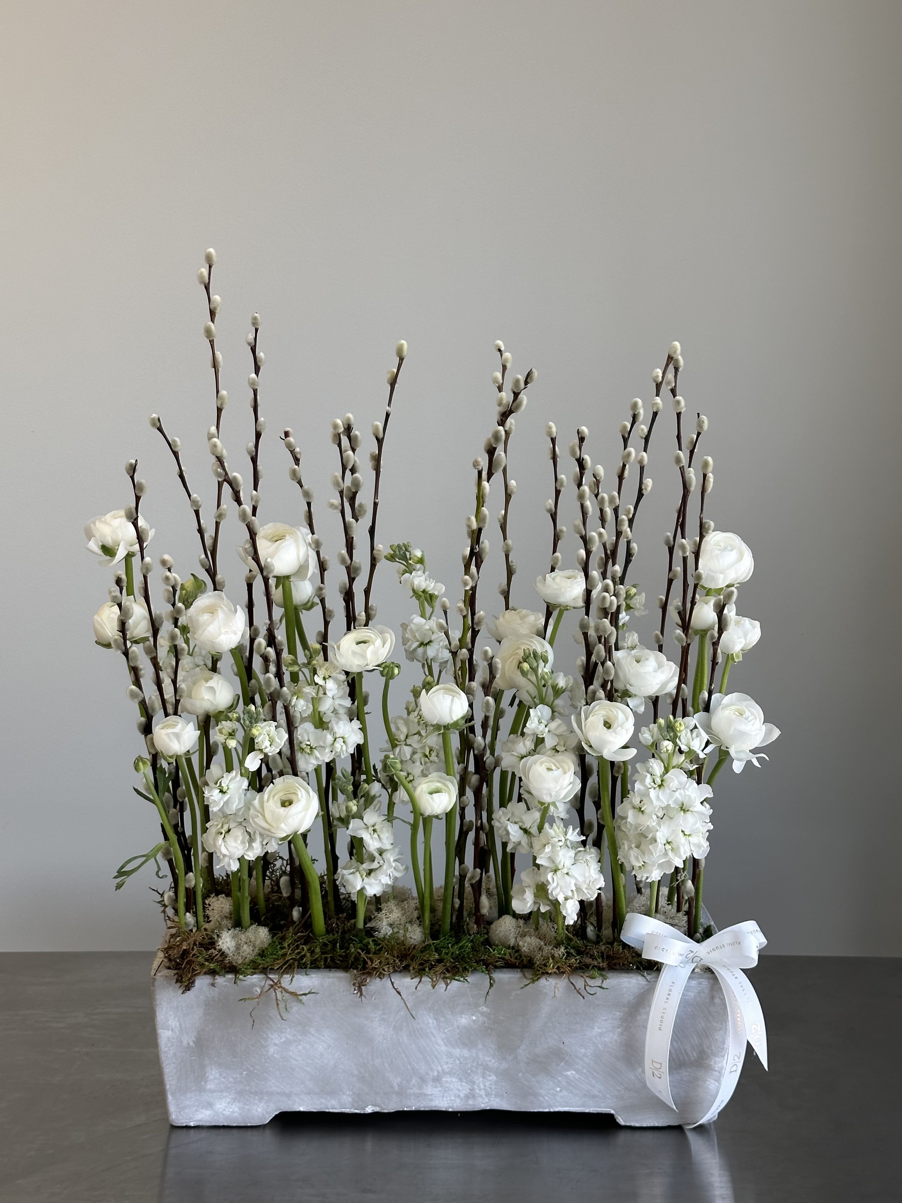 White floral arrangement with tall pussy willow branches in a rectangular container