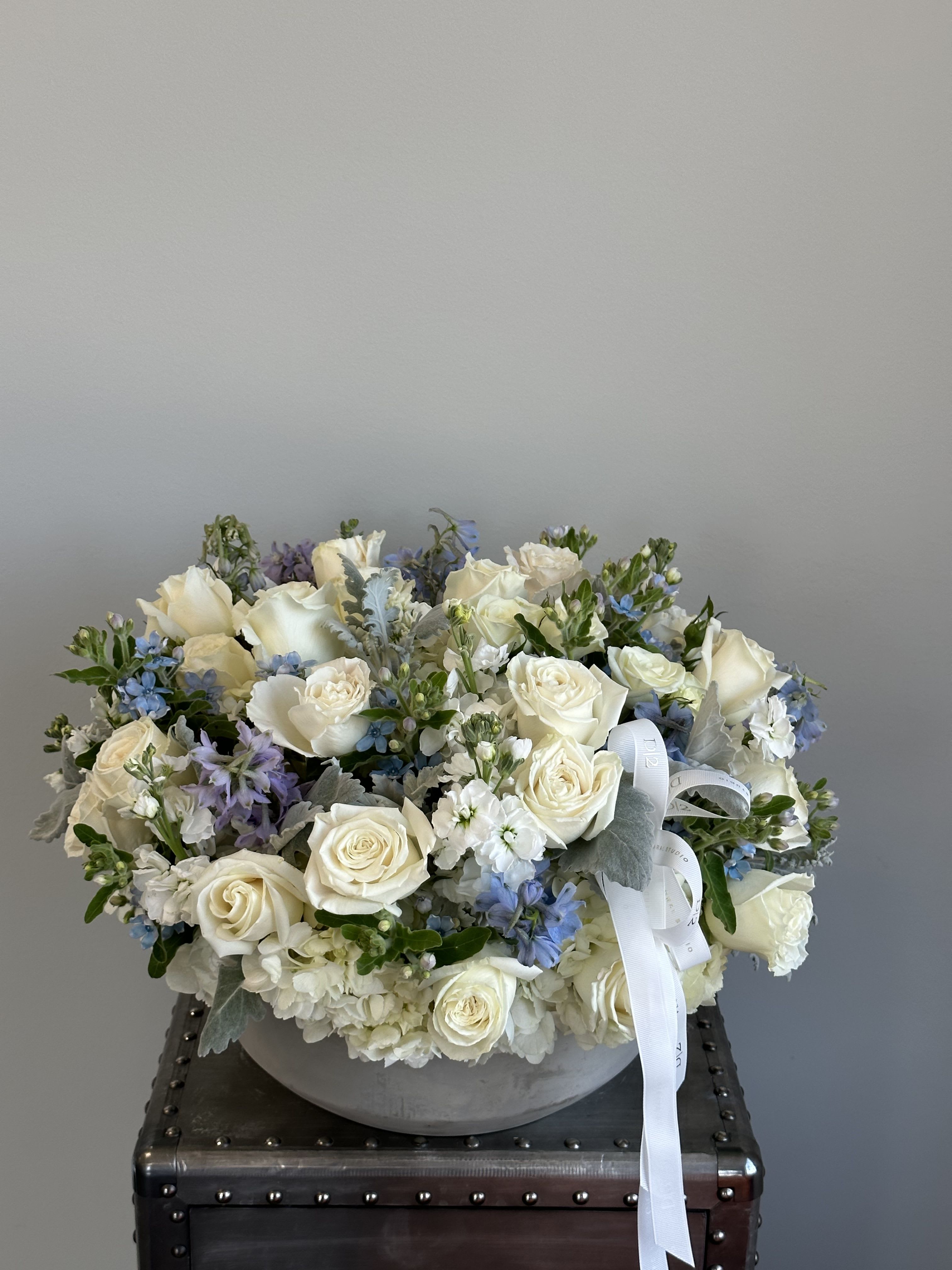 White rose and blue flower arrangement in a round gray vase