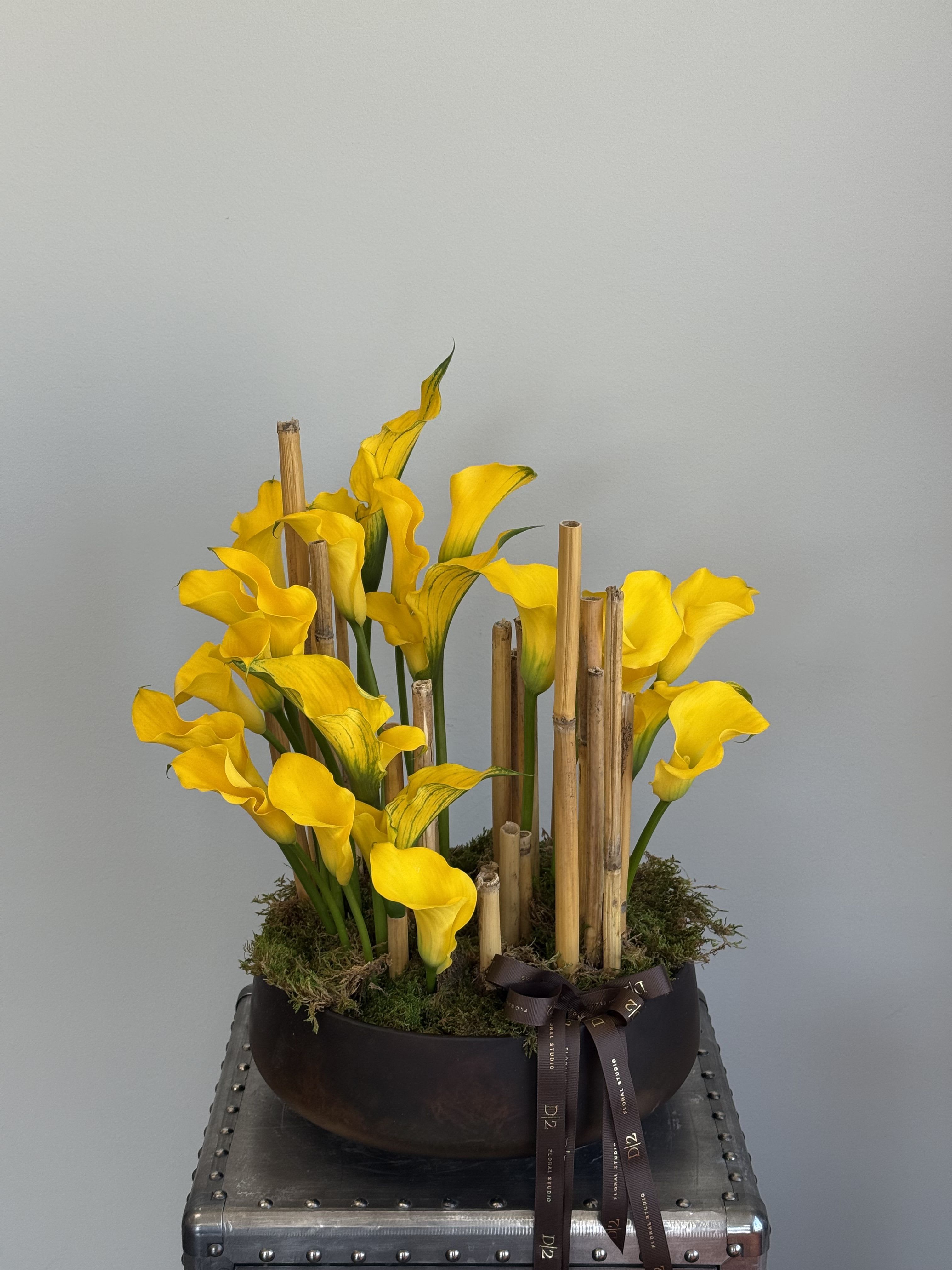 Yellow calla lilies arranged in a low black bowl with bamboo accents