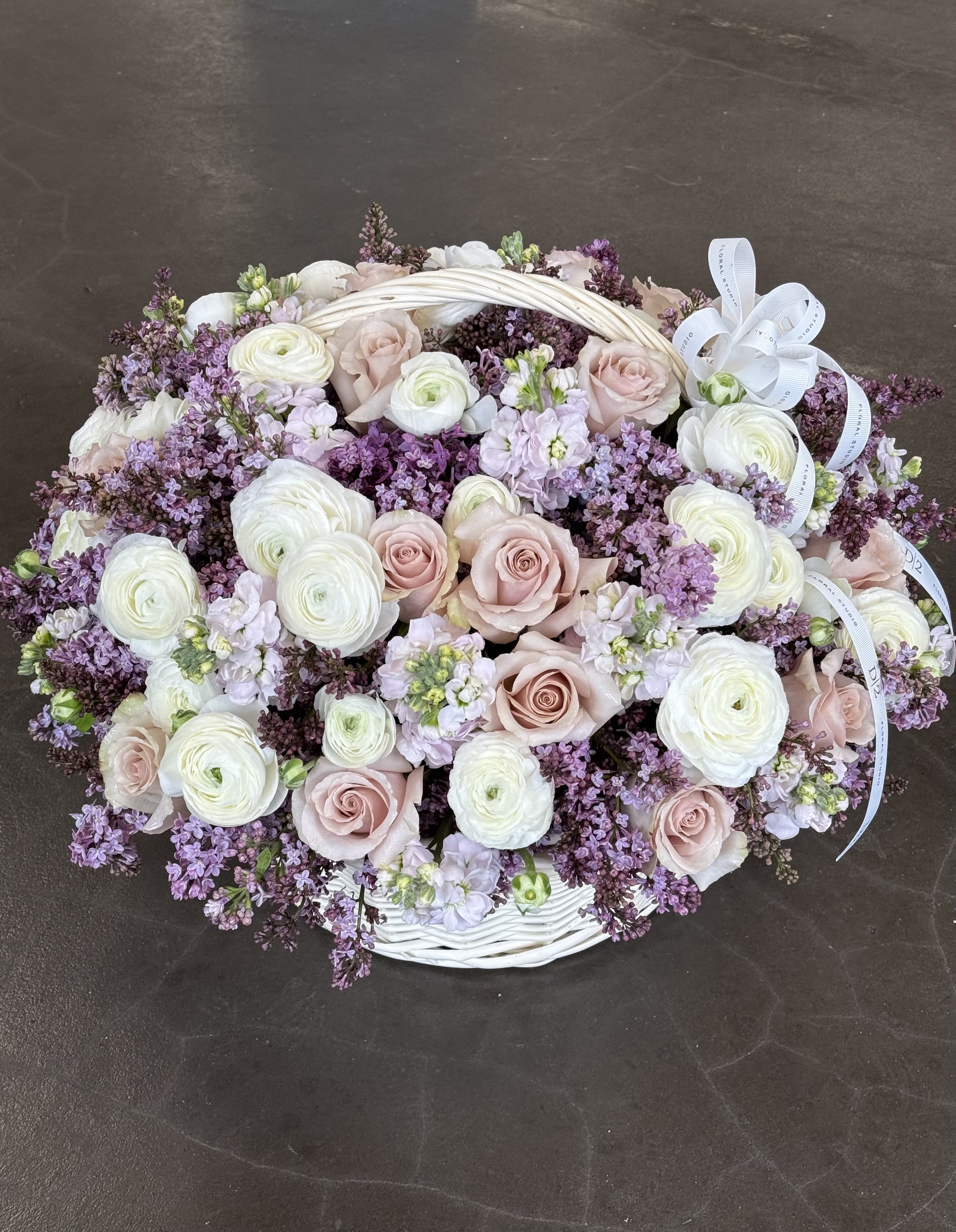 Oval basket arrangement of pale pink roses and white ranunculus with lavender filler