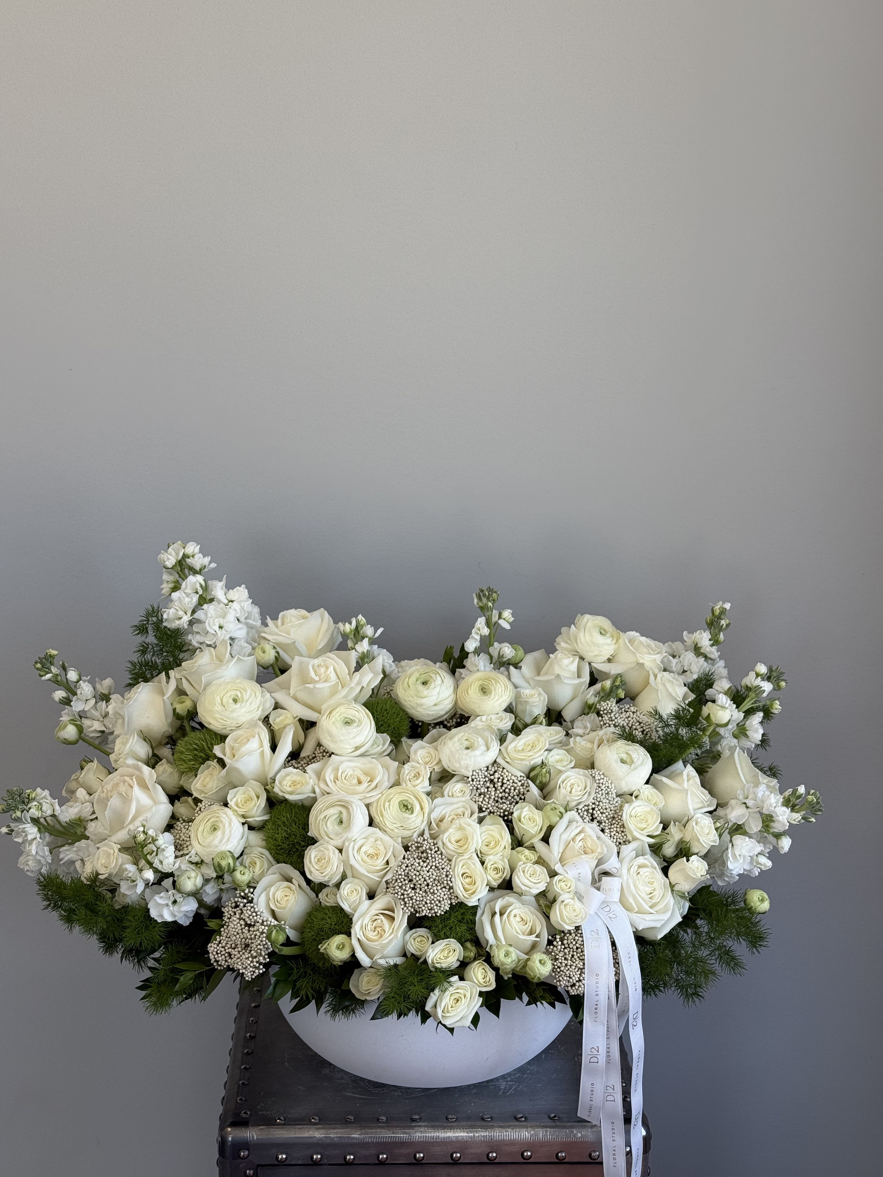 Large white rose arrangement in a low white bowl with trailing ribbon