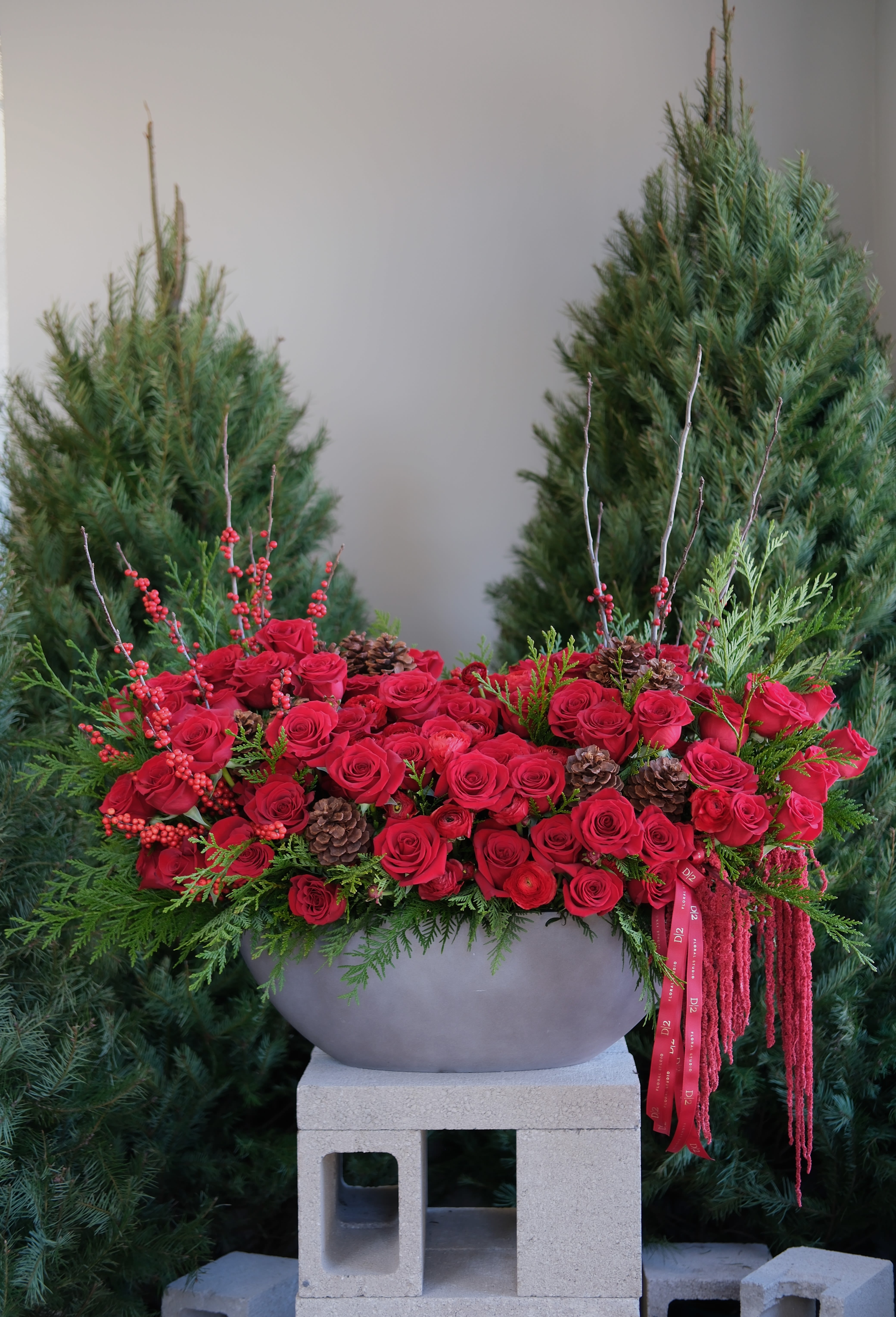 Red rose arrangement in a gray bowl with pinecones and berries