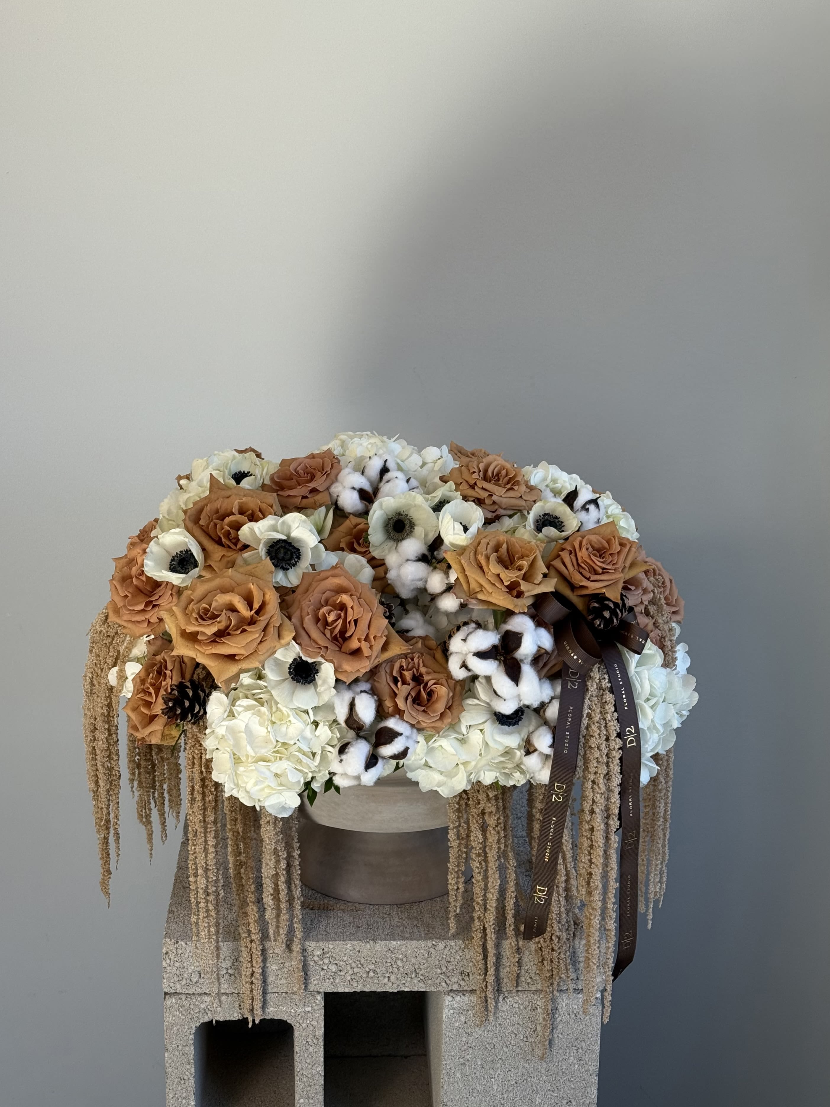 Large arrangement of tan roses, white blooms, and cotton stems in a round container
