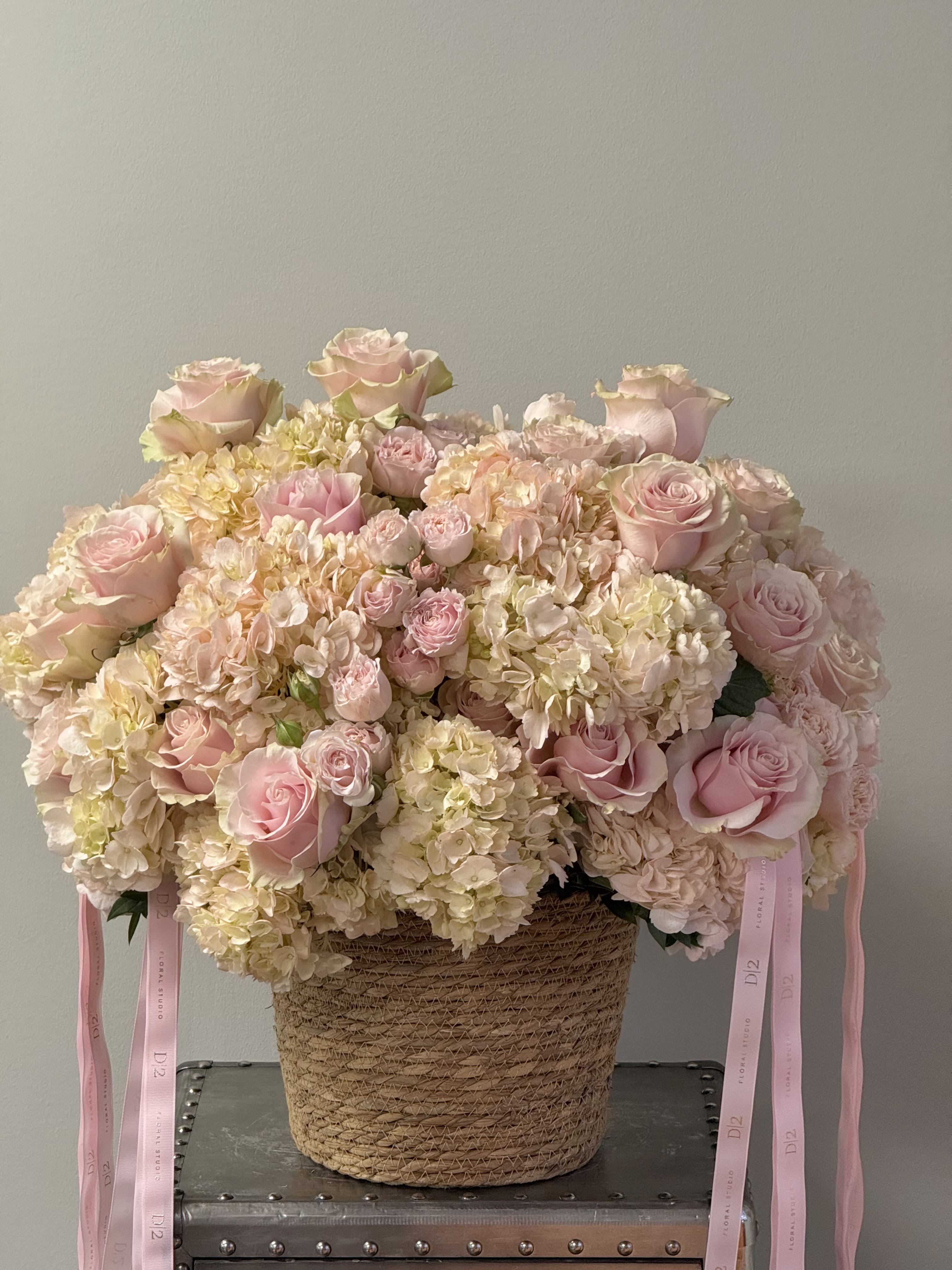Pink roses and hydrangeas in a woven basket with ribbon tails