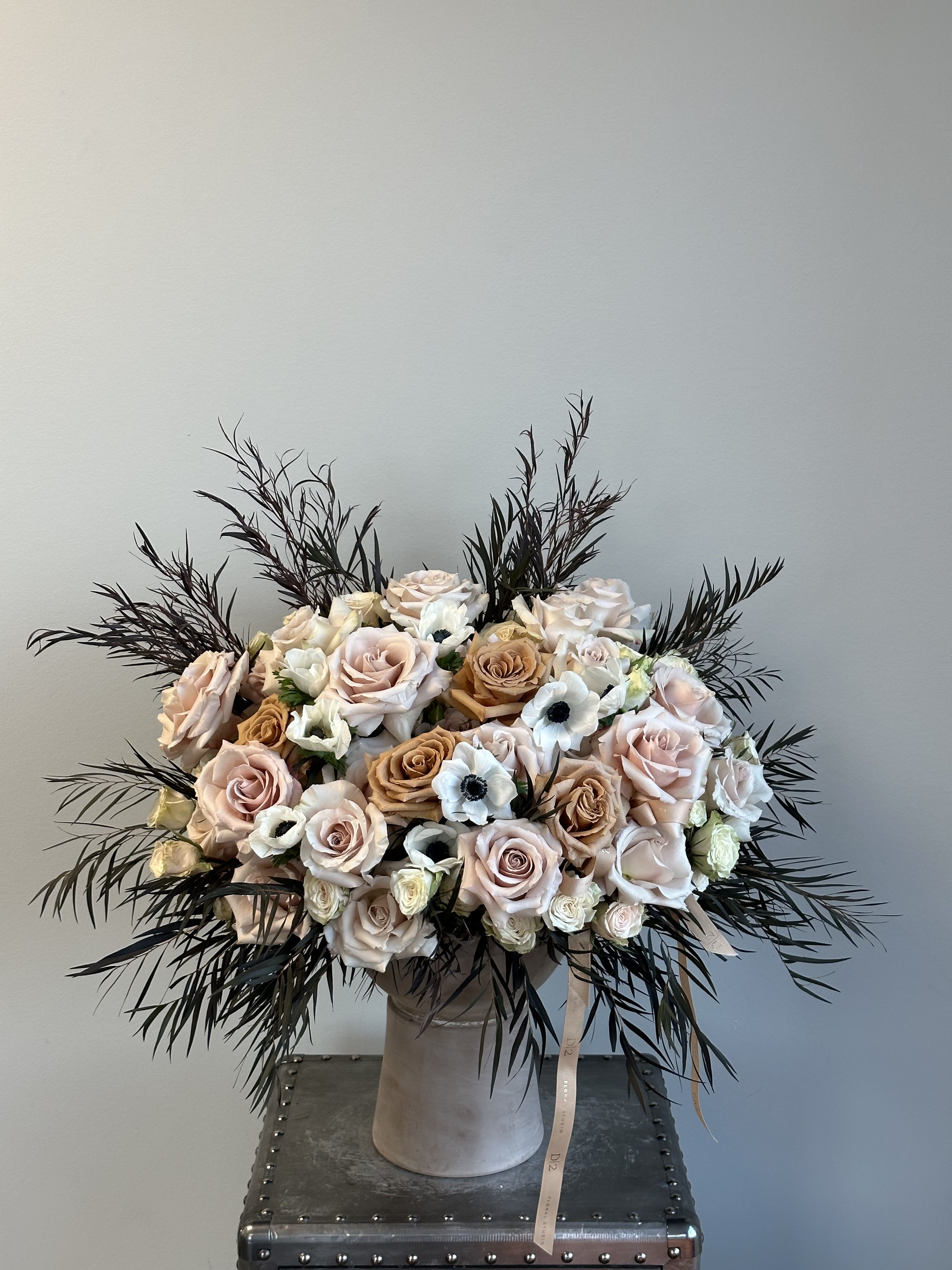 Blush and ivory rose bouquet in a tall vase with dark feathery foliage