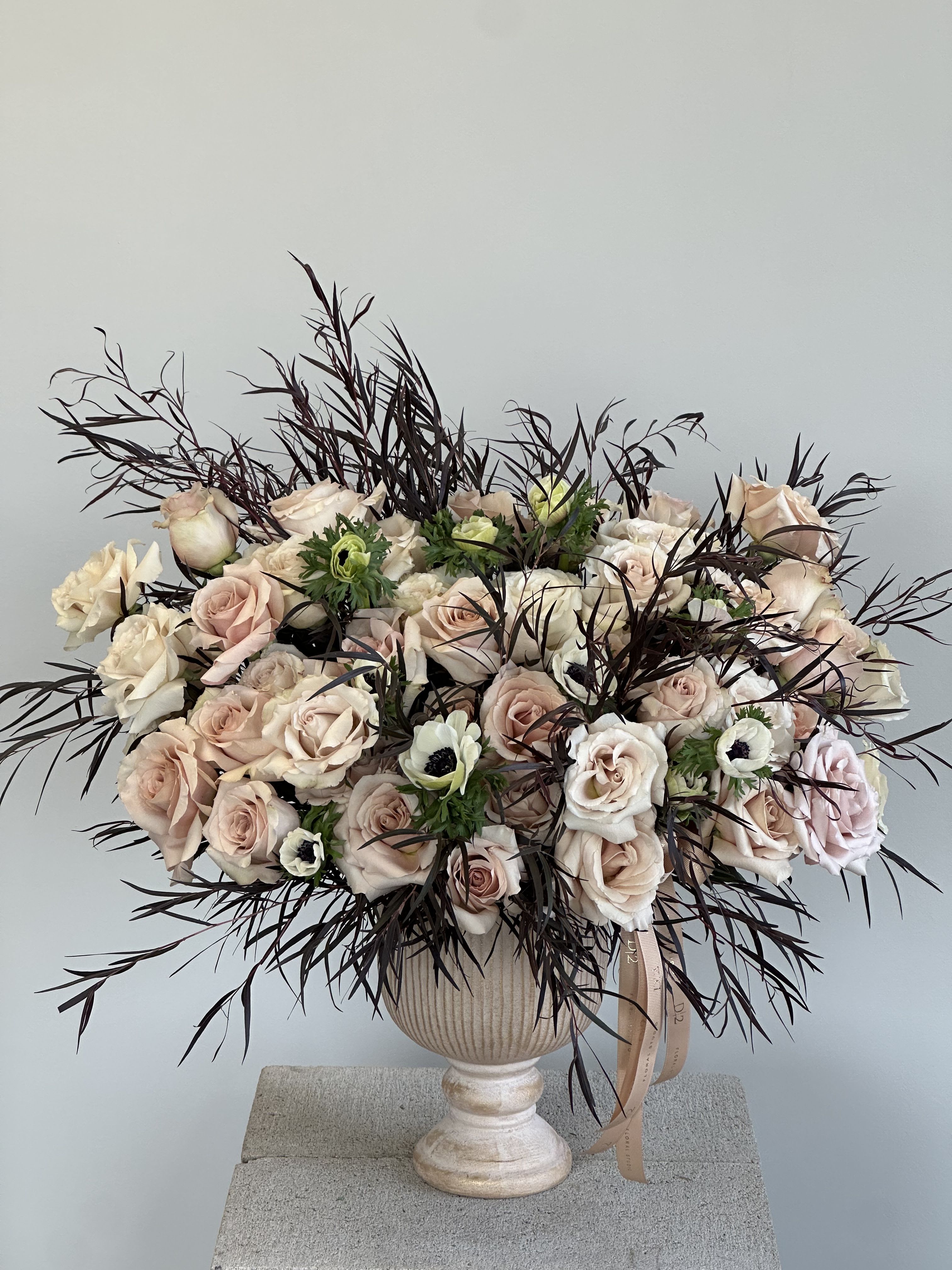Velvet Whisper - Lush arrangement of soft blush roses and delicate anemones, accented with airy dark foliage, elegantly presented in a timeless pedestal vase for a refined, modern look.