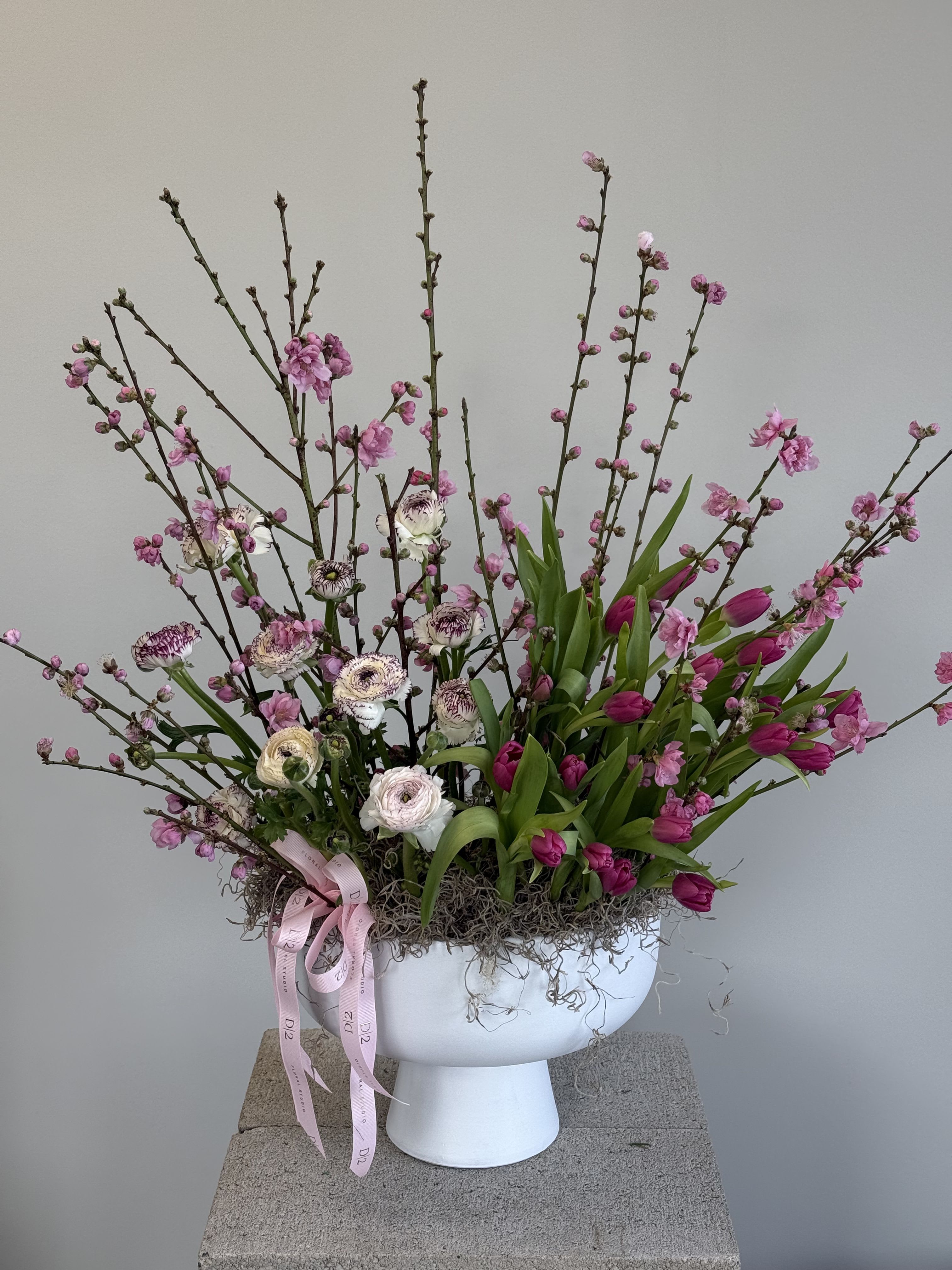 Pink blossoms and tulips in a white pedestal vase