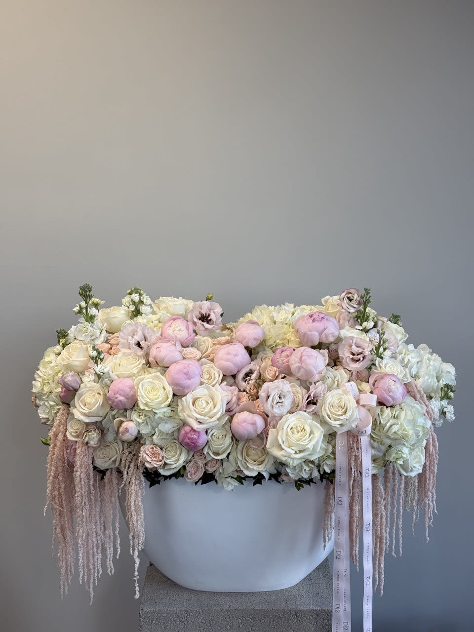 Large pastel floral arrangement in a white container with trailing ribbons