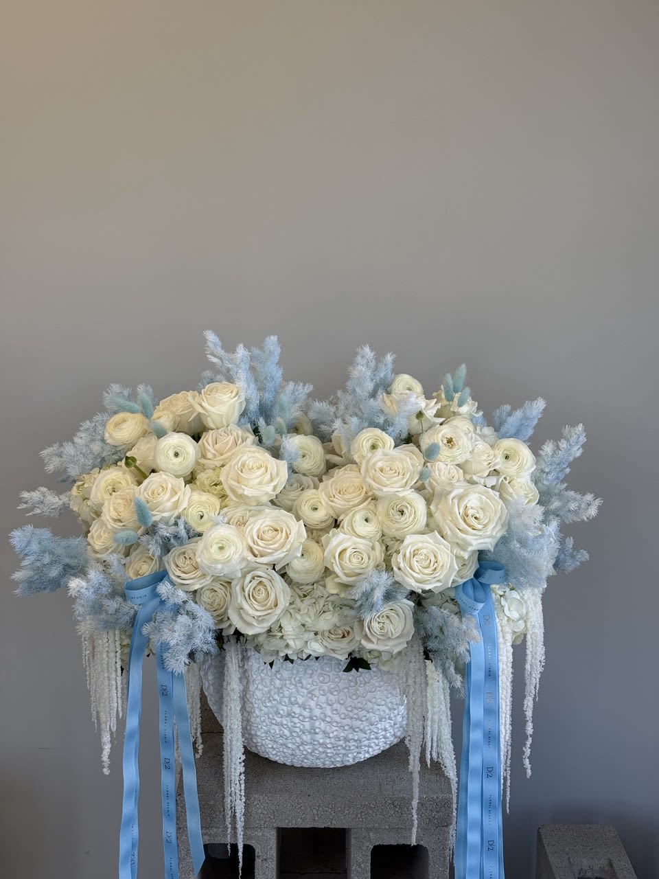 Large white rose arrangement with pale blue accents in a textured vase